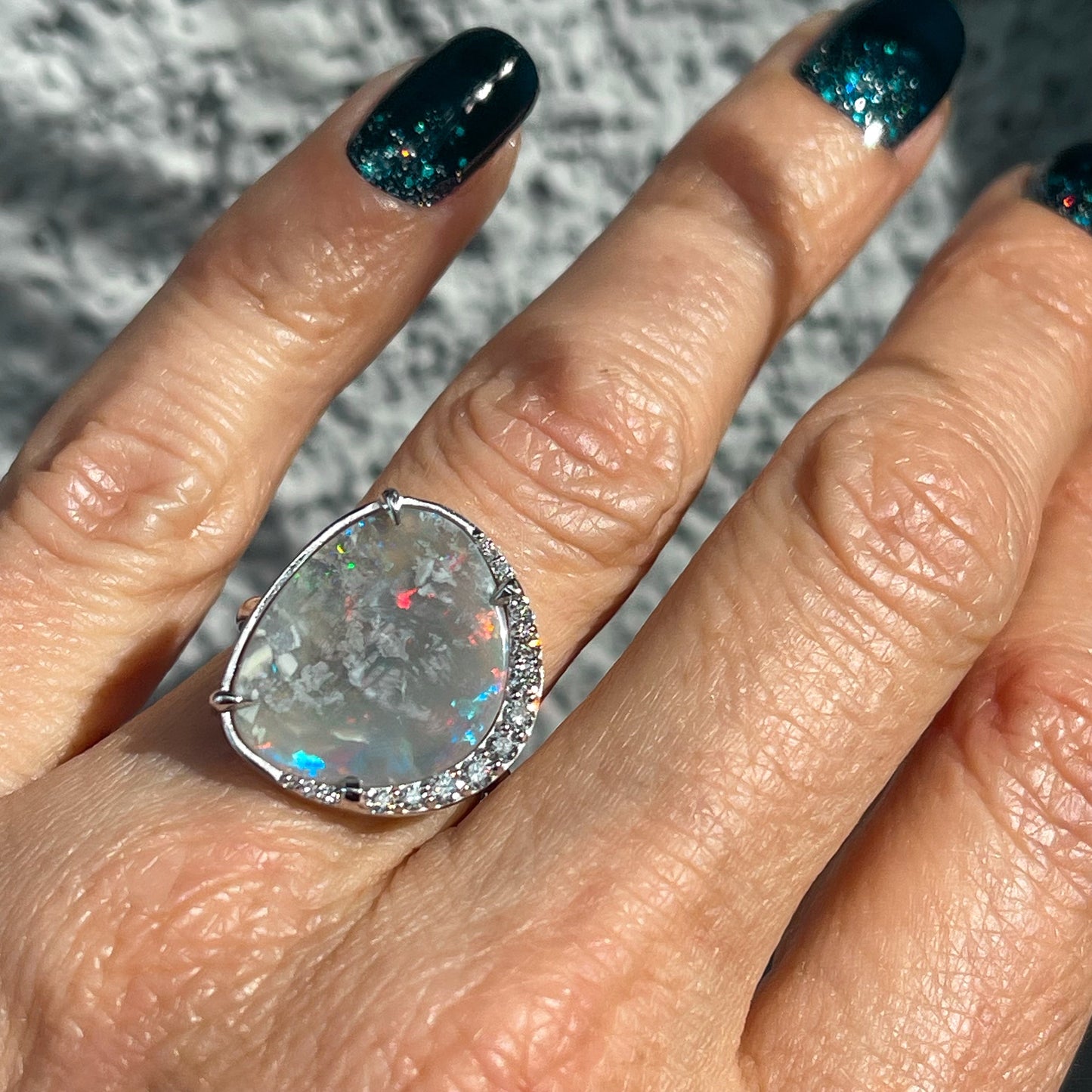 An Australian Opal Ring by NIXIN Jewelry. The opal and diamond ring is modeled on a hand.