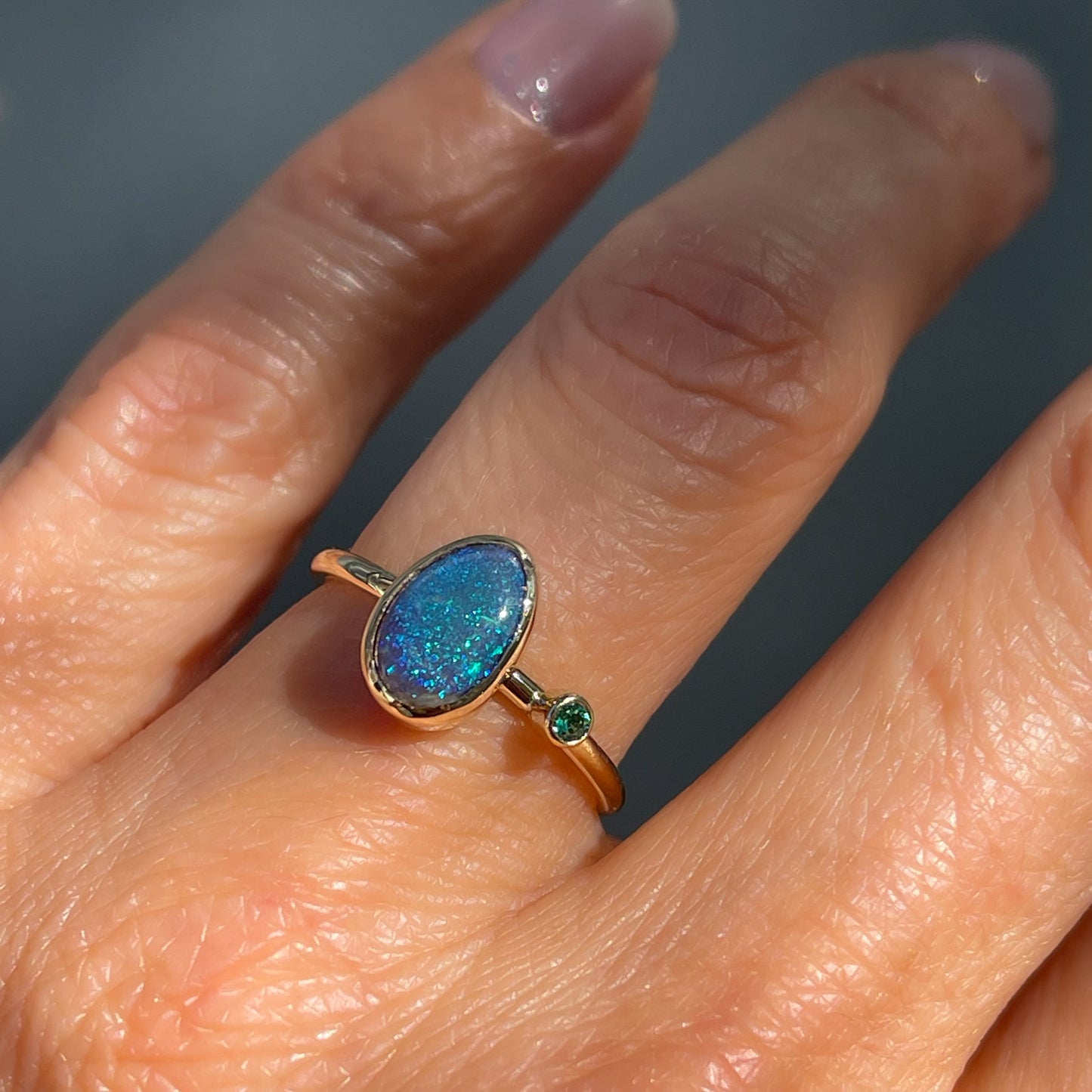 An Australian Opal Ring by NIXIN Jewelry modeled on a hand. A black opal and emerald luxury ring.