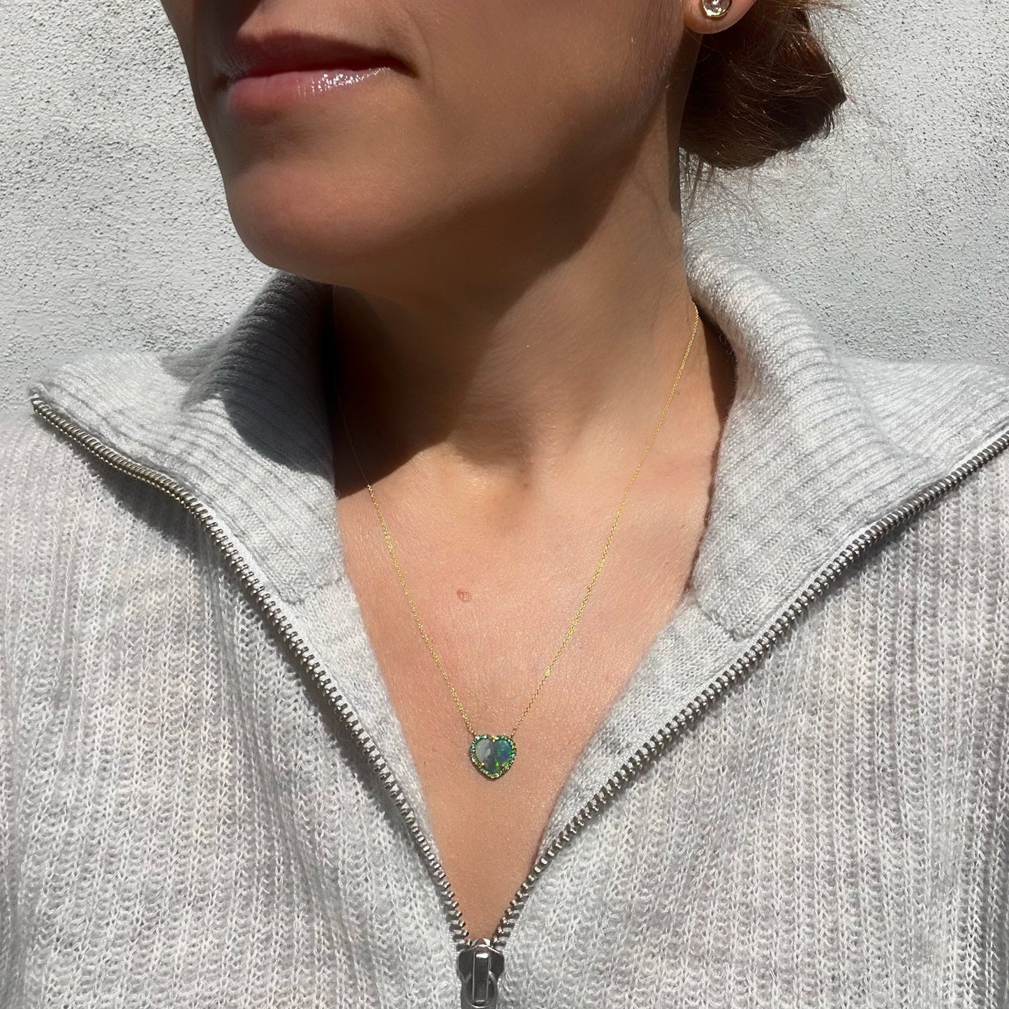A model is wearing an Australian Opal Heart Necklace by NIXIN Jewelry. The gold opal necklace has a heart shaped Black Opal surrounded by emeralds.