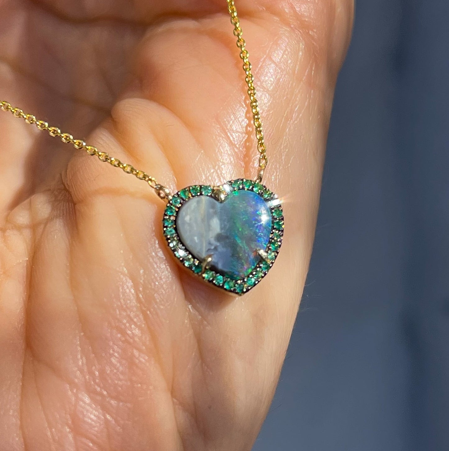 An Australian Opal Heart Necklace by NIXIN Jewelry rests on a hand. The Australian Opal necklace reflects sun off its emerald halo.