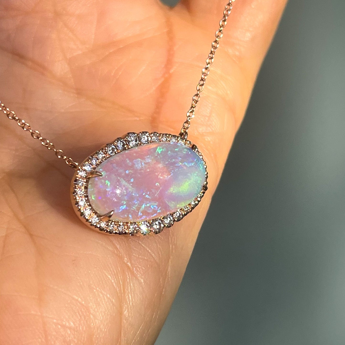 An Australian Opal Necklace by NIXIN Jewelry shot at an angle and resting against a hand. The purple opal is set east west and secured by prong setting.
