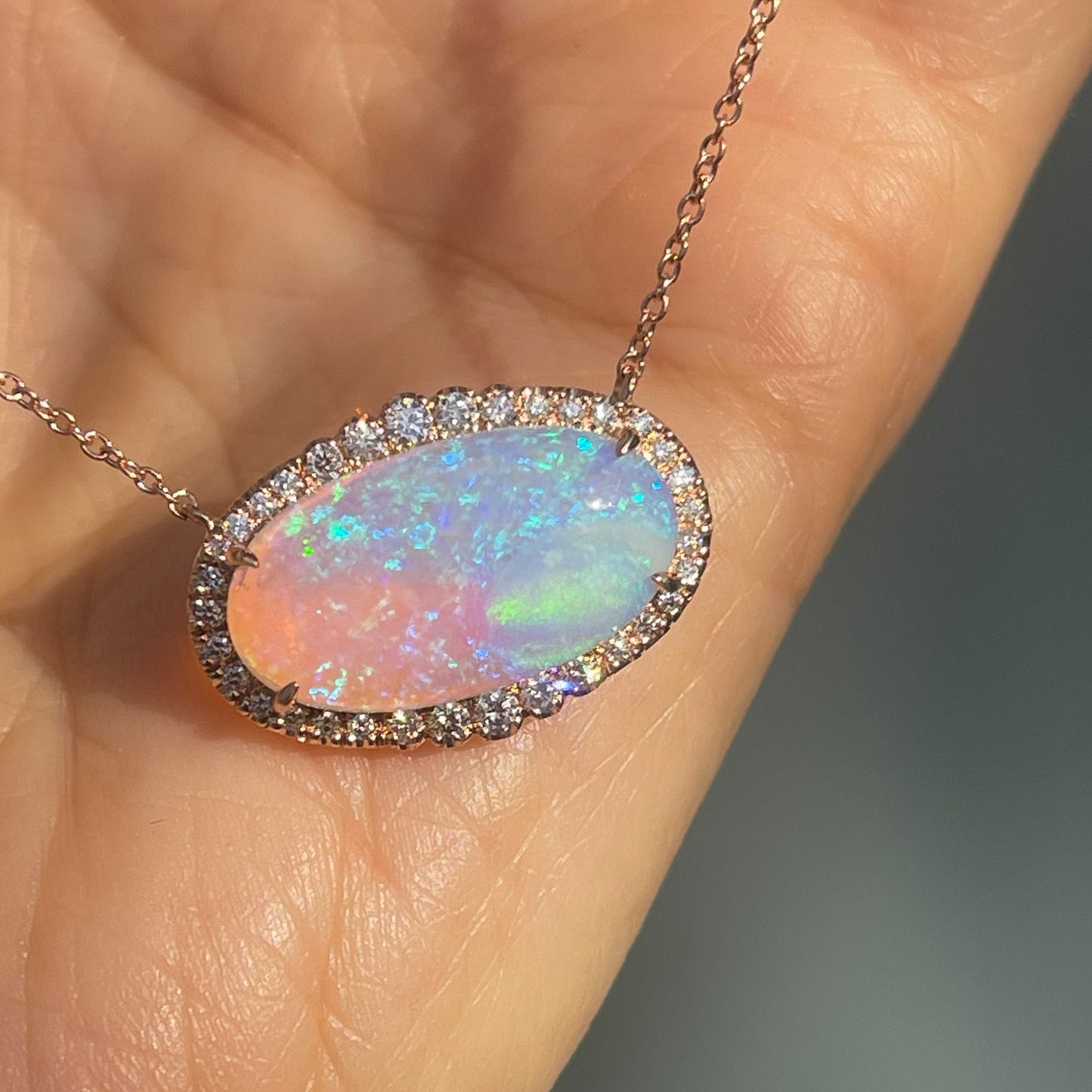 An Australian Opal Necklace by NIXIN Jewelry resting upon a hand. The opal and diamond necklace is set in 14k rose gold.