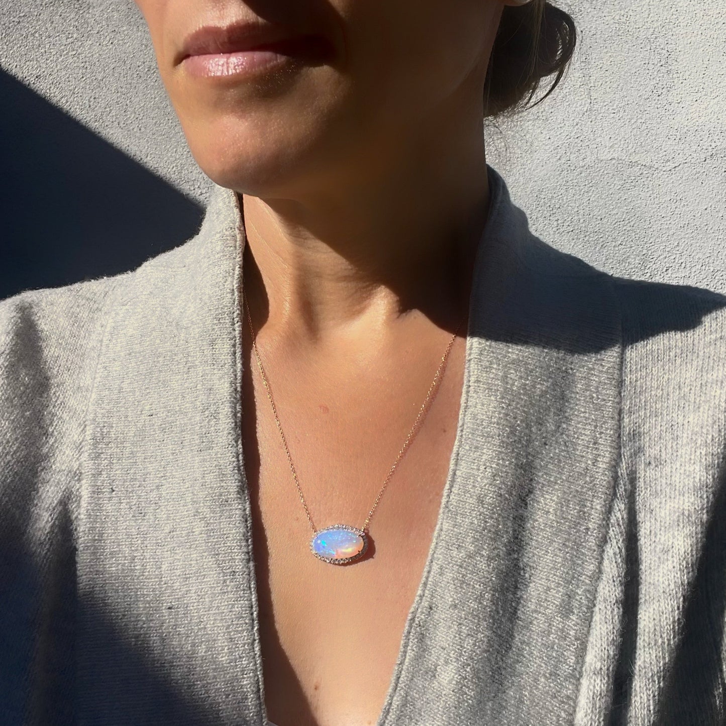 An Australian Opal Necklace by NIXIN Jewelry worn by a model. Set in rose gold with a diamond halo, the opal necklace hangs at 18 inches.