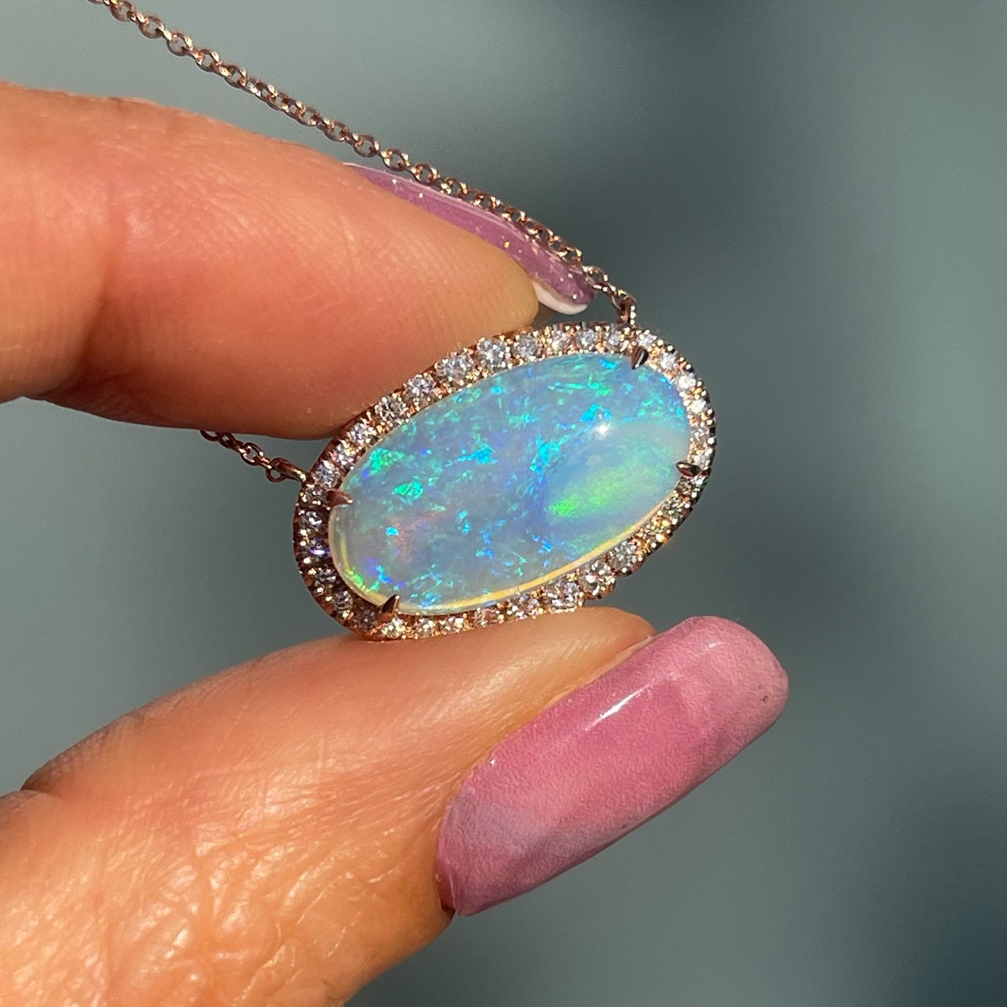 An Australian Opal Necklace held up in sunlight. Image displays blue and green opal fire and pave diamond halo.