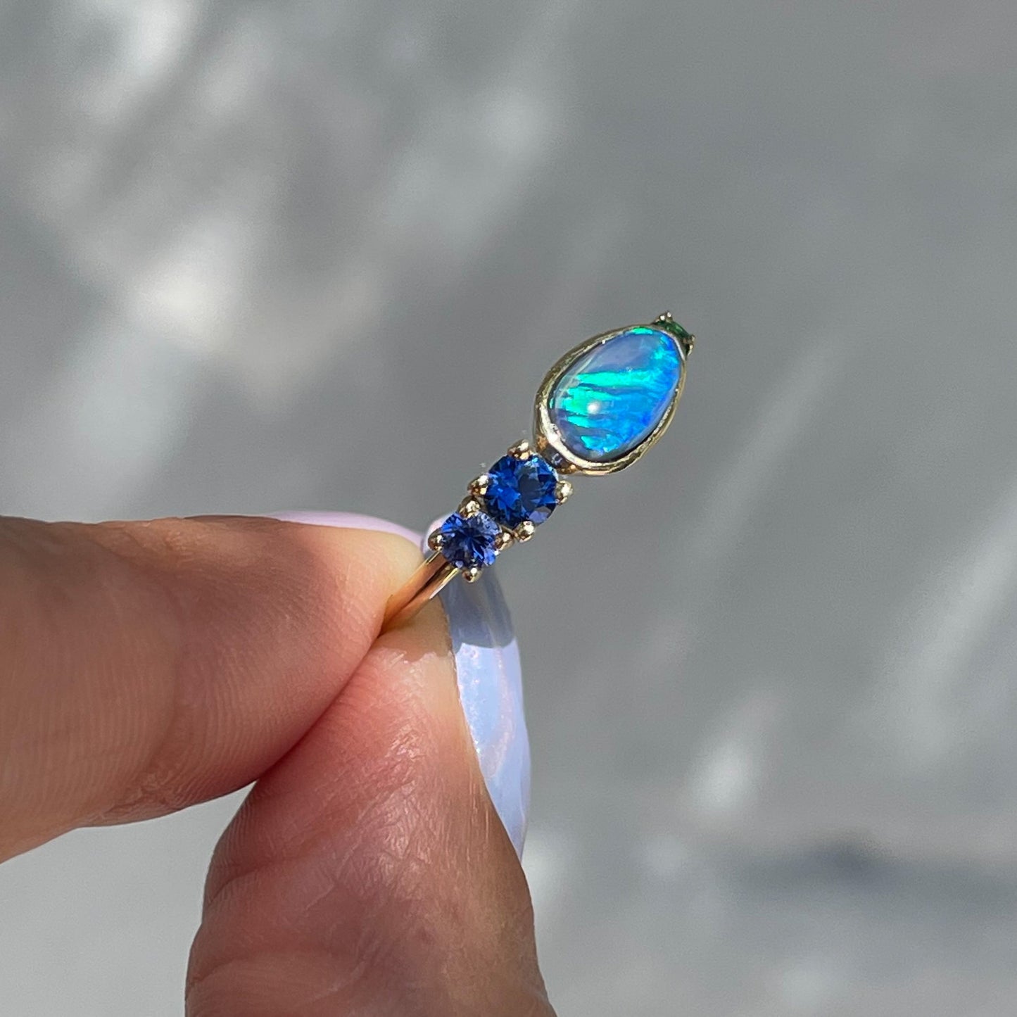 Black Opal Ring by NIXIN Jewelry held showing side. Gold opal ring with sapphires.