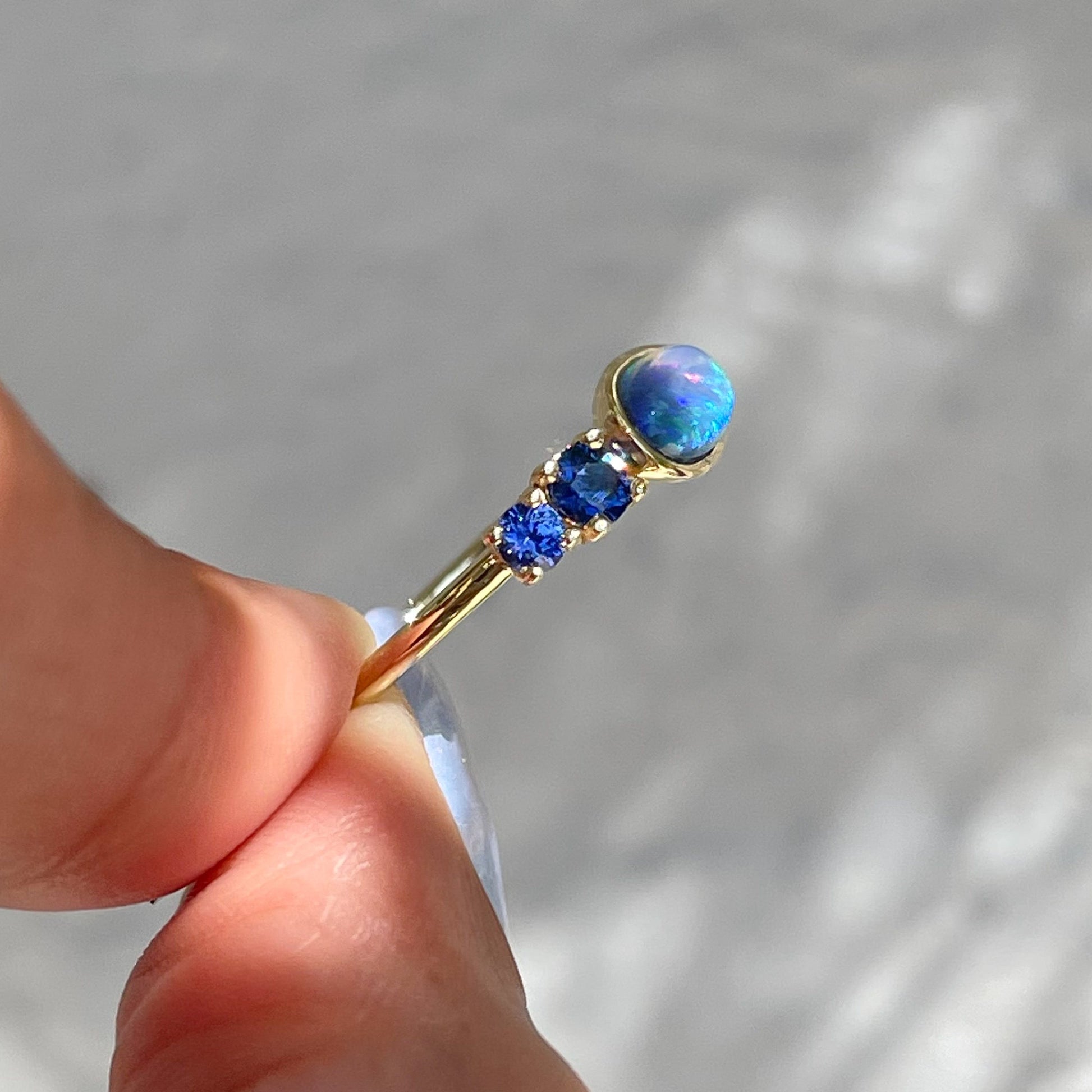 Black Opal Ring by NIXIN Jewelry held showing side view. Blue sapphire and opal ring.