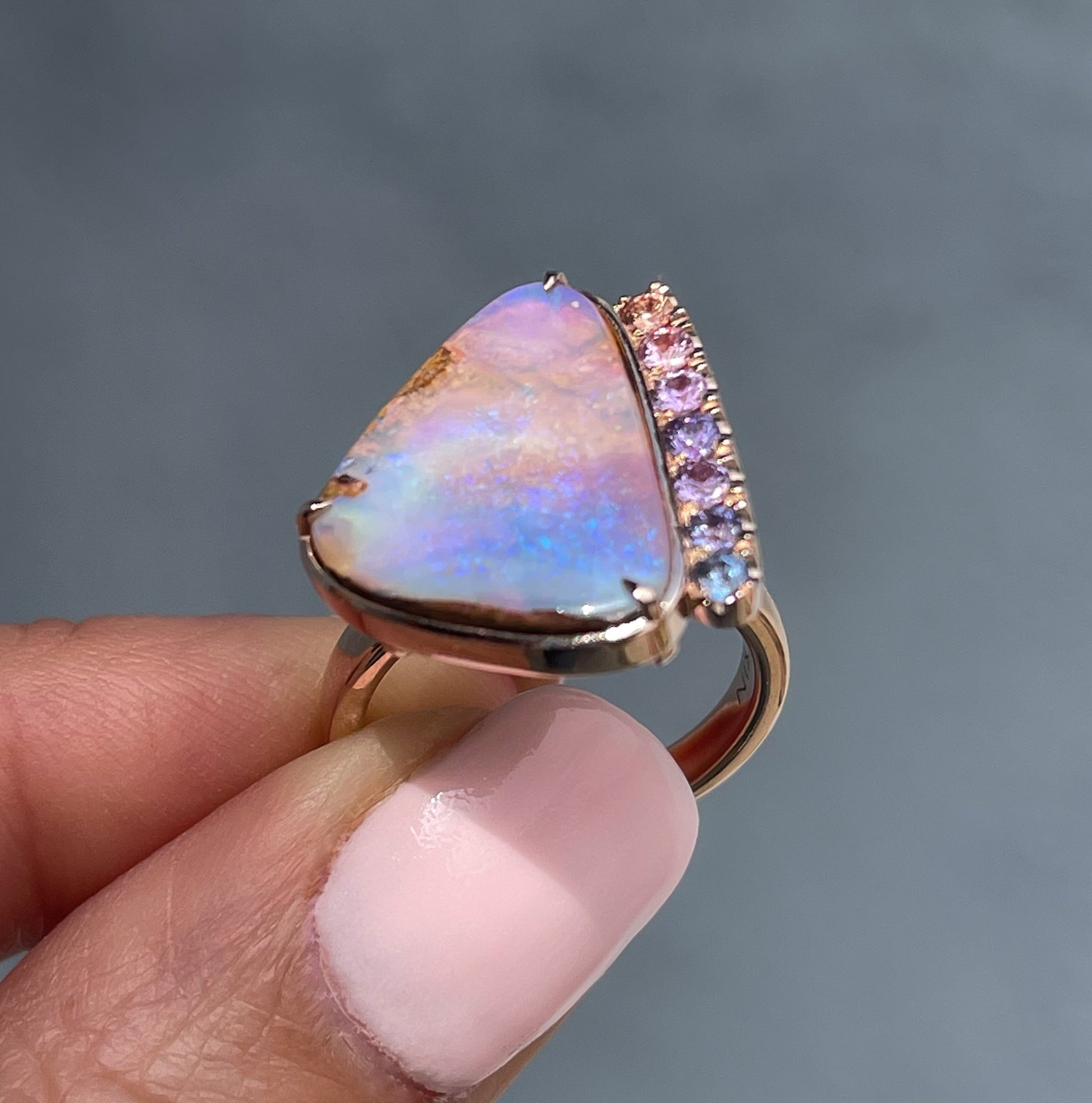Angled shot of an Australian Opal Ring by NIXIN Jewelry. A 14k rose gold ring made with a natural opal and pink sapphires.