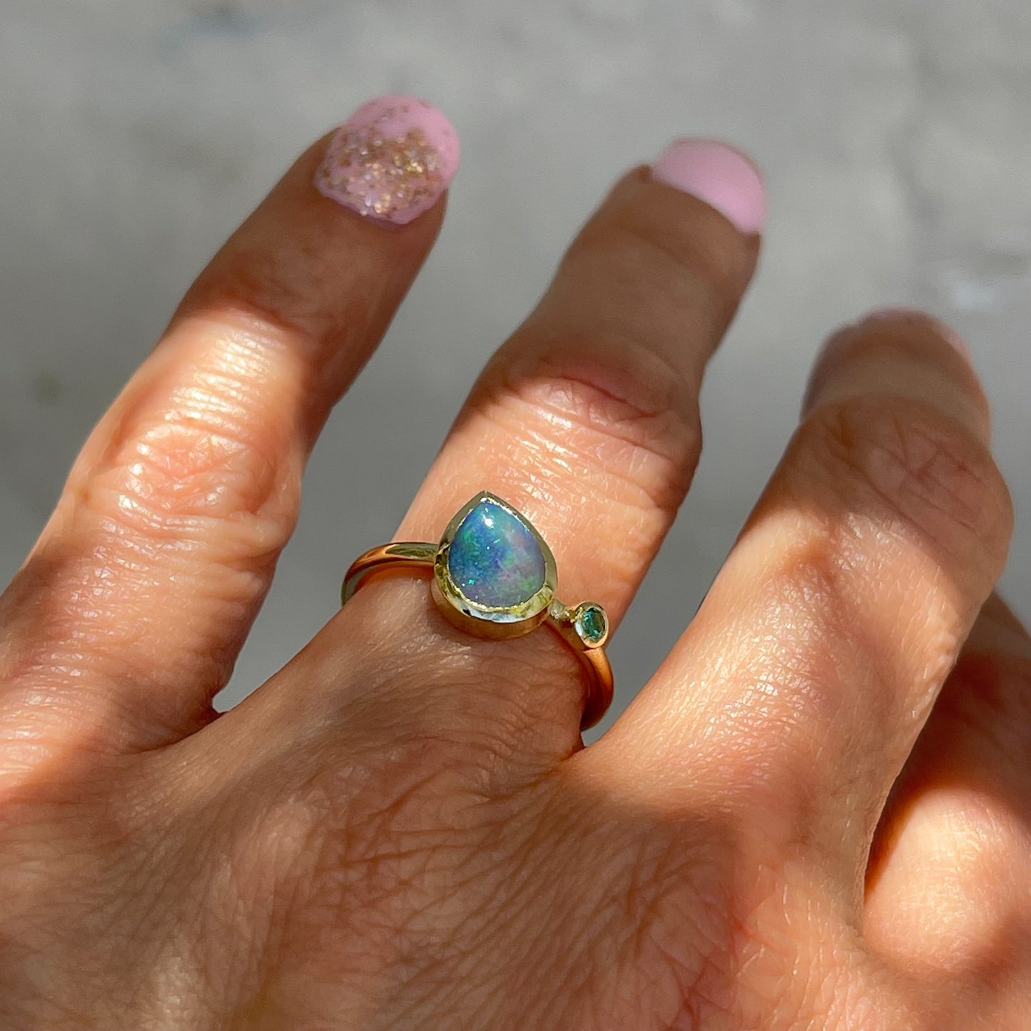 An Australian Opal Ring by NIXIN Jewelry modeled on the hand. Made with a Black Opal and a small emerald.