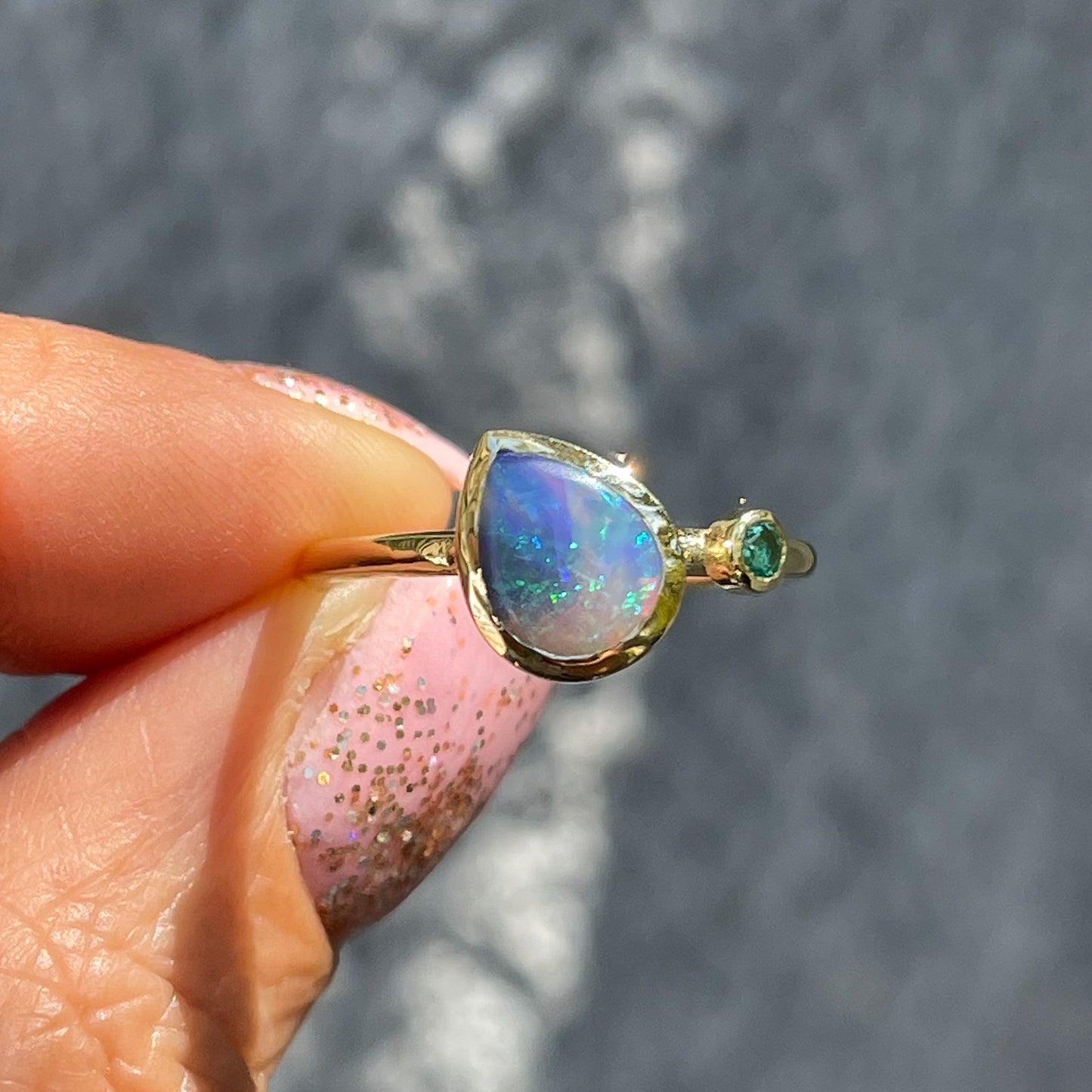An Australian Opal Ring by NIXIN Jewelry held in sunlight. A natural opal ring made with a Black Opal.