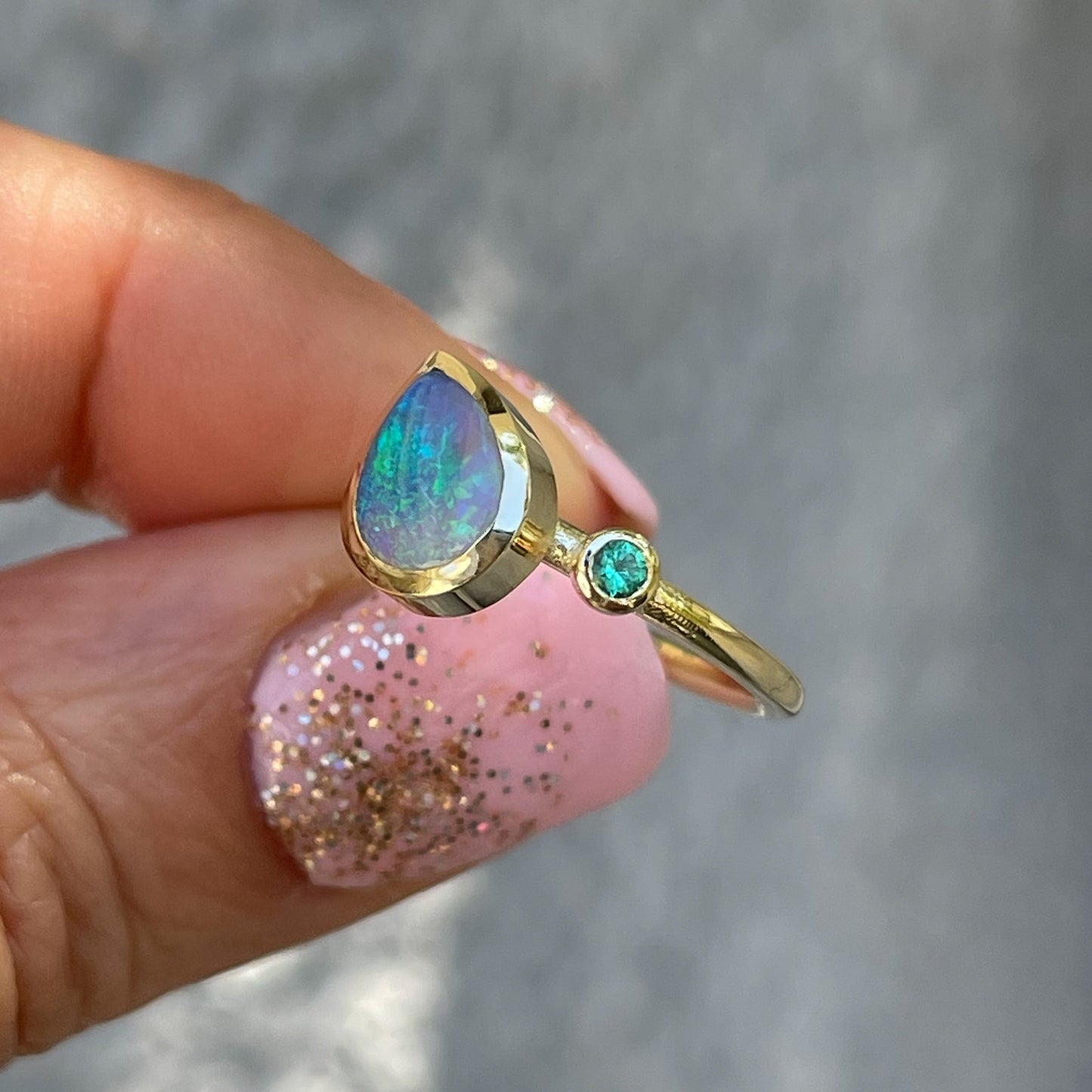 An Australian Opal Ring by NIXIN Jewelry held at an angle to display its bezel setting. An emerald and Lightning Ridge Black Opal Ring.