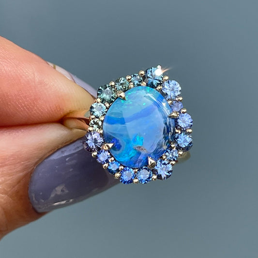 Australian Opal Ring by NIXIN Jewelry held in front of glass door. Sapphire and opal ring.