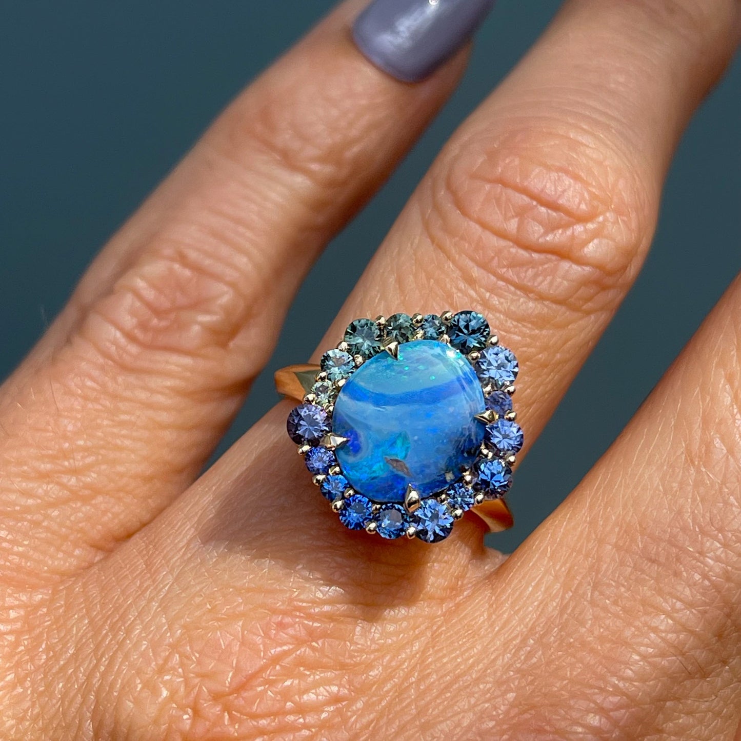 Australian Opal Ring by NIXIN Jewelry modeled on hand. Opal and sapphire ring with an asymmetrical halo.