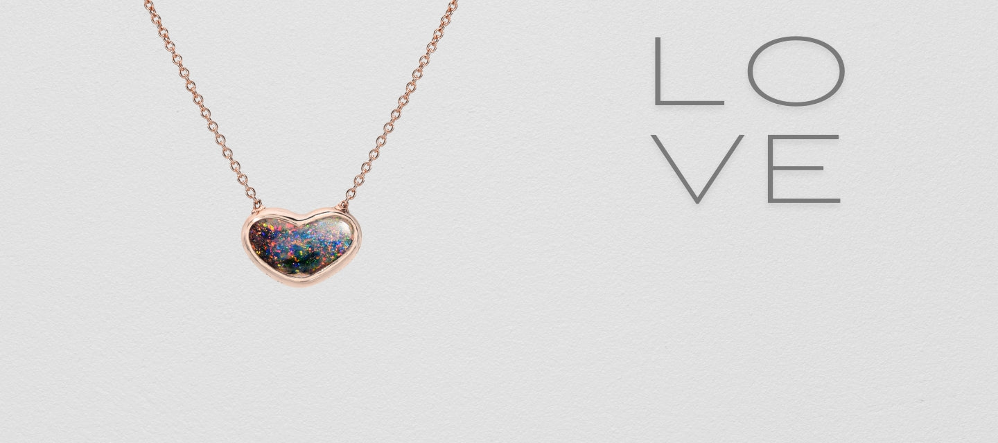 An Australian Opal Necklace by NIXIN Jewelry with a black opal set in rose gold. The opal necklace has a tiny opal heart with red play of color. It's a two sided opal.