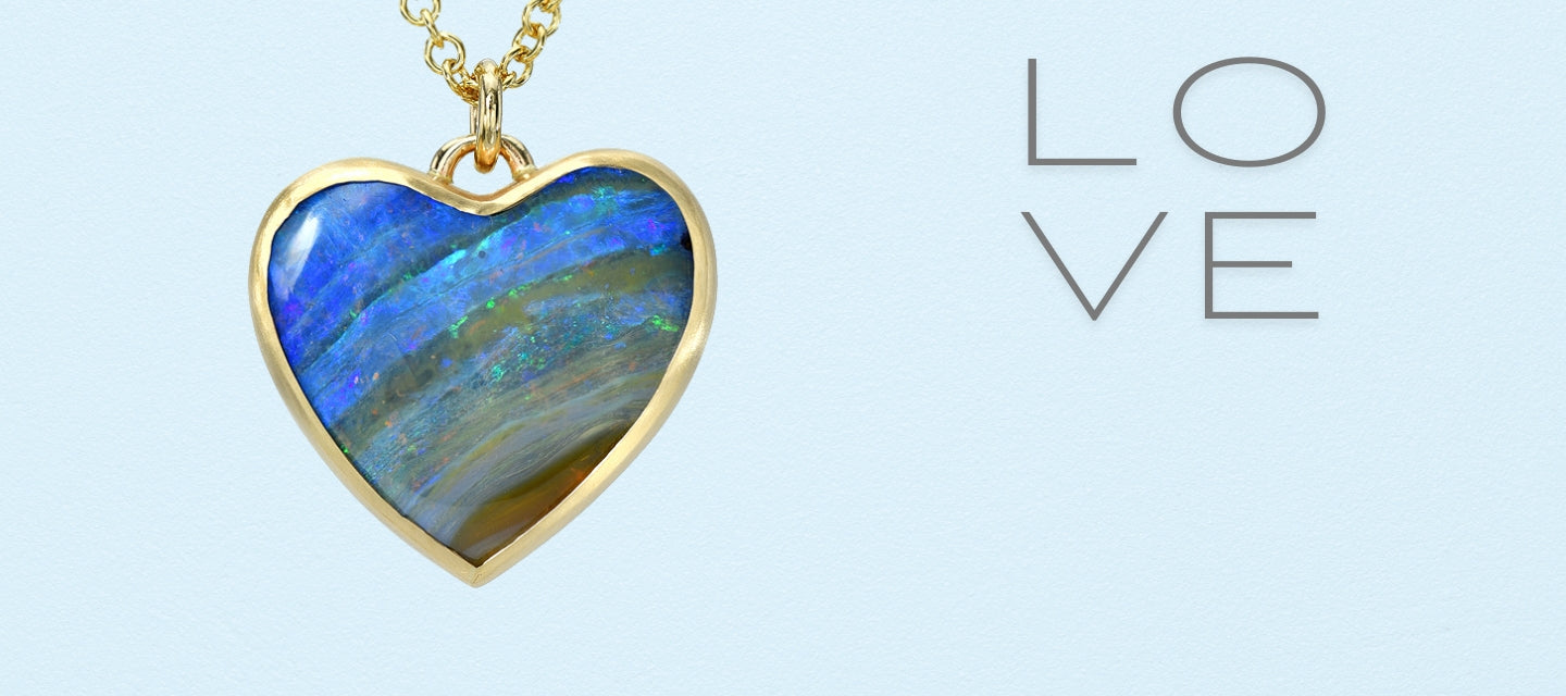 An Australian Opal Pendant on a pale blue backdrop. The opal heart necklace is made with a boulder opal in a gold bezel setting.