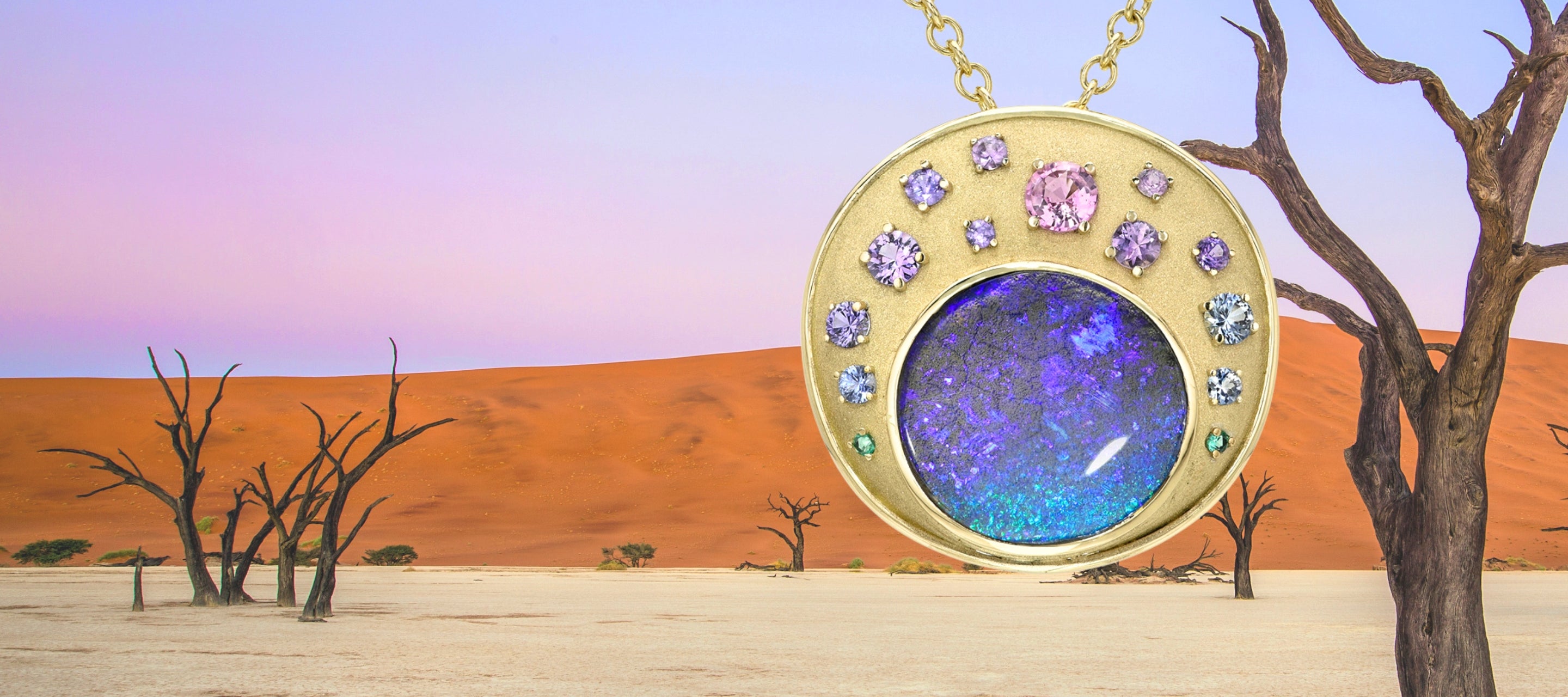 An 18 gold Australian Opal Necklace by NIXIN Jewelry, with a boulder opal, sapphires and emeralds shown hanging in front of a desert background.