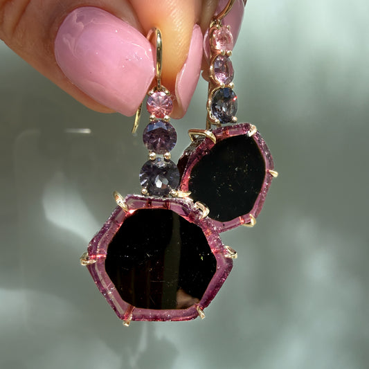 Eclipsed Tourmaline Drop Earrings held at the fingertips, a pair of bi-color tourmaline slice earrings in 14k gold with sapphire and spinel.
