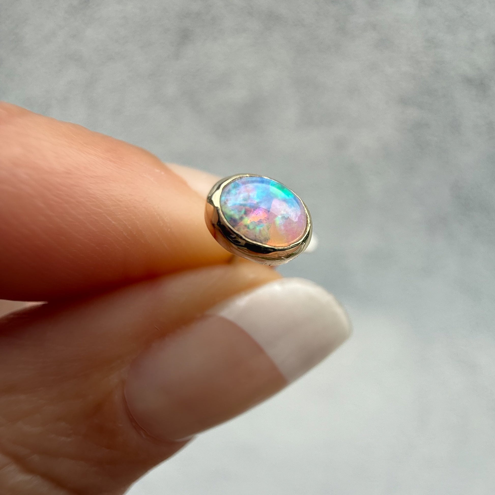 Australian Opal Earrings by NIXIN Jewelry. Close-up of the larger single opal stone set in 14k gold, showcasing its pink and blue iridescence (or color play). Shop our selection of luxury opal jewelry and fine opal stud earrings.