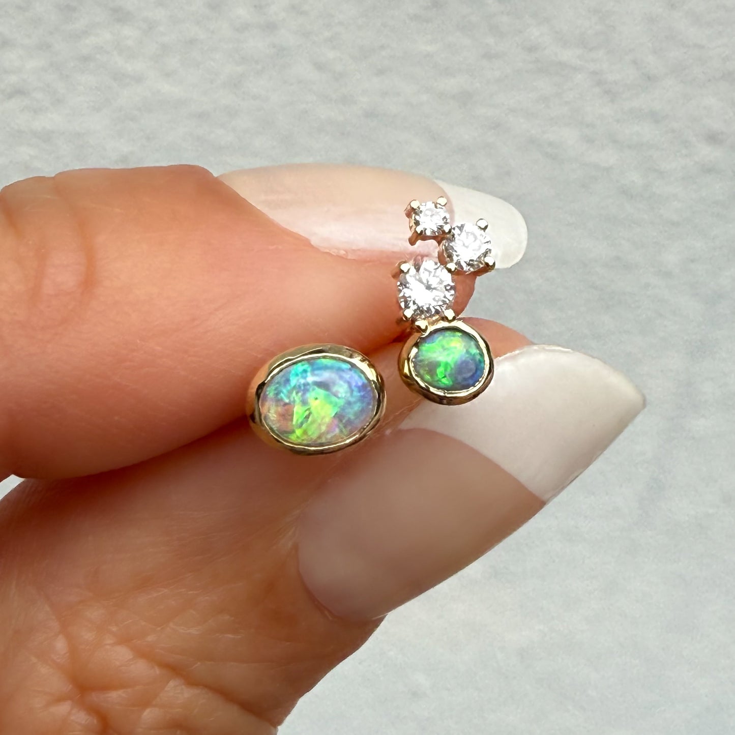 Australian Opal Earrings by NIXIN Jewelry. The smaller opal stud features a cluster of diamonds and a black opal in a 14k gold bezel. This opal diamond earrings design elevates opal jewelry to true luxury.