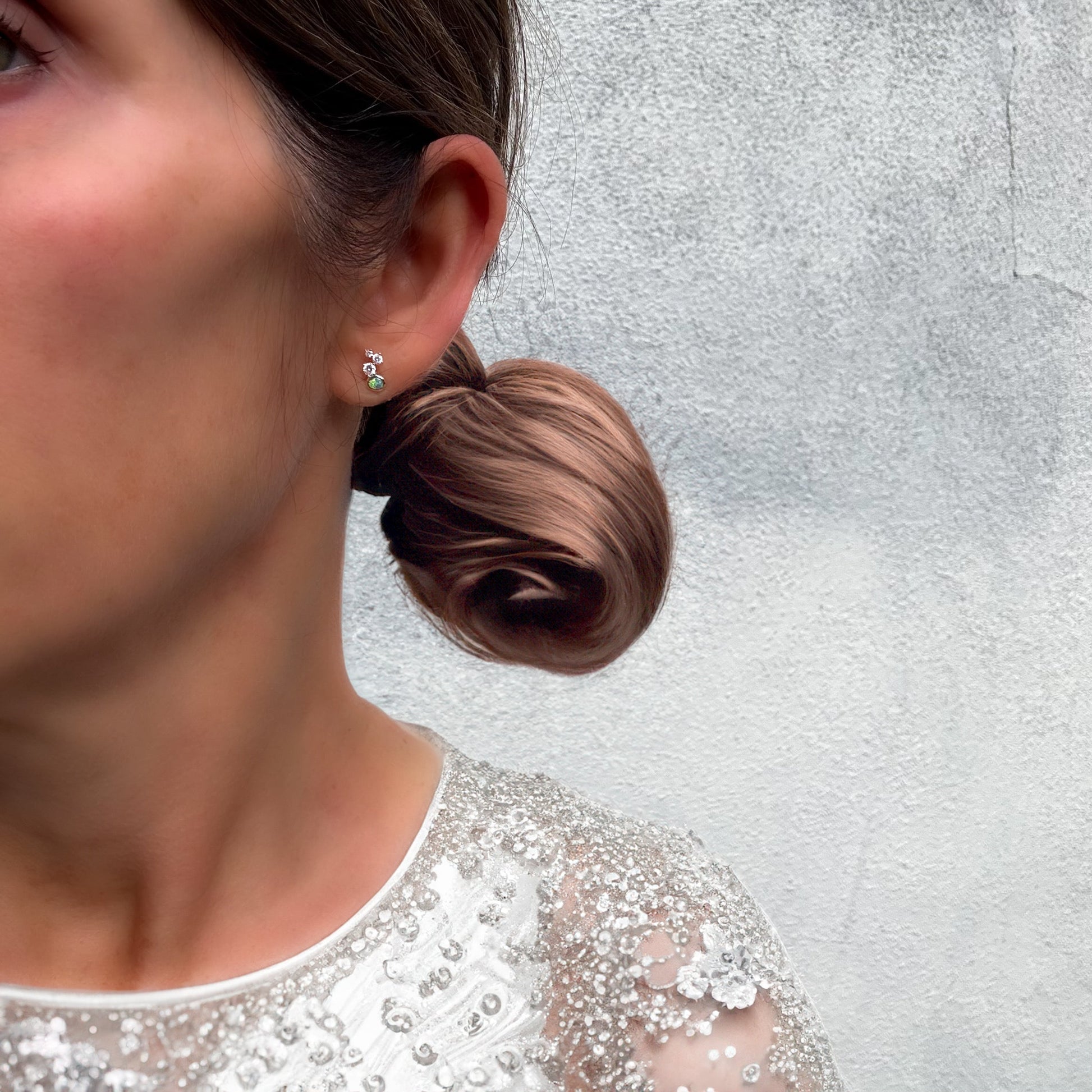 Australian Opal Earrings by NIXIN Jewelry. Model wearing the opal studs, showing the scale of the mismatched earrings as unique fine jewelry. This black opal earrings set is a wearable piece of art and rare jewelry.