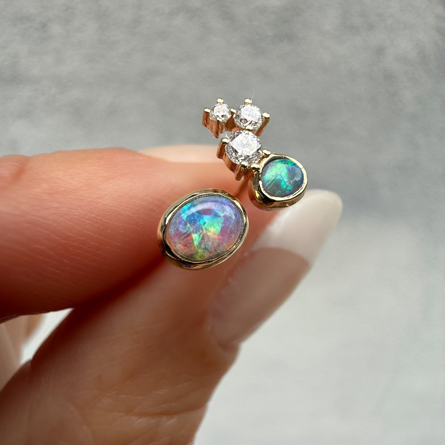 Australian Opal Earrings by NIXIN Jewelry. Handheld view of the stunning 14k gold opal studs with black crystal opal. This opal jewelry is the perfect statement art piece, blending opals and diamonds beautifully.