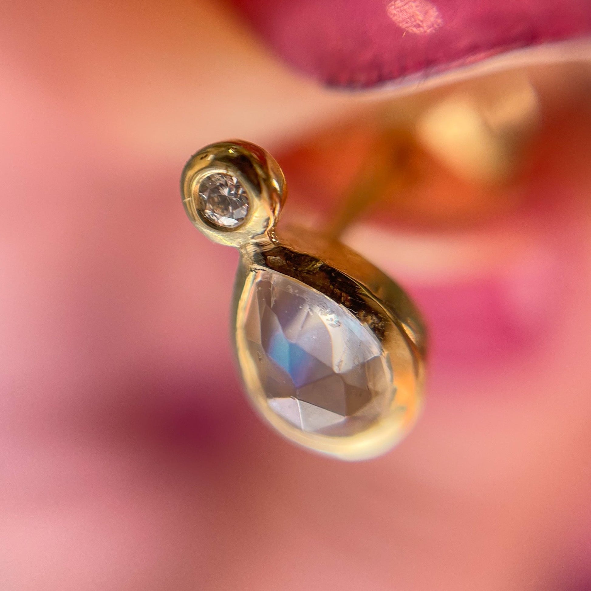 Moonstone Earrings by NIXIN Jewelry shown under magnification. One stud earring is shot at an angle, displaying the rose cut moonstone and small diamond.