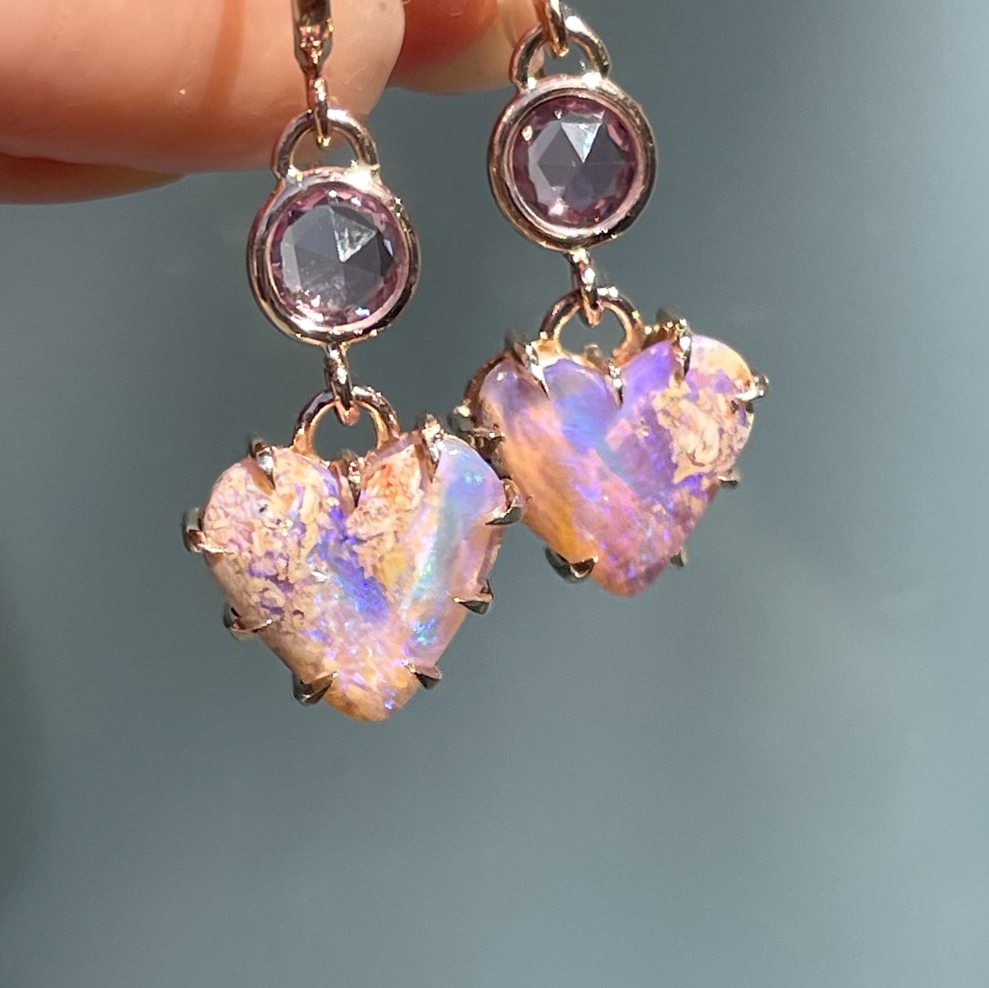 A pair of Australian Opal Earrings by NIXIN Jewelry. The Australian opals dangle below two purple sapphires.