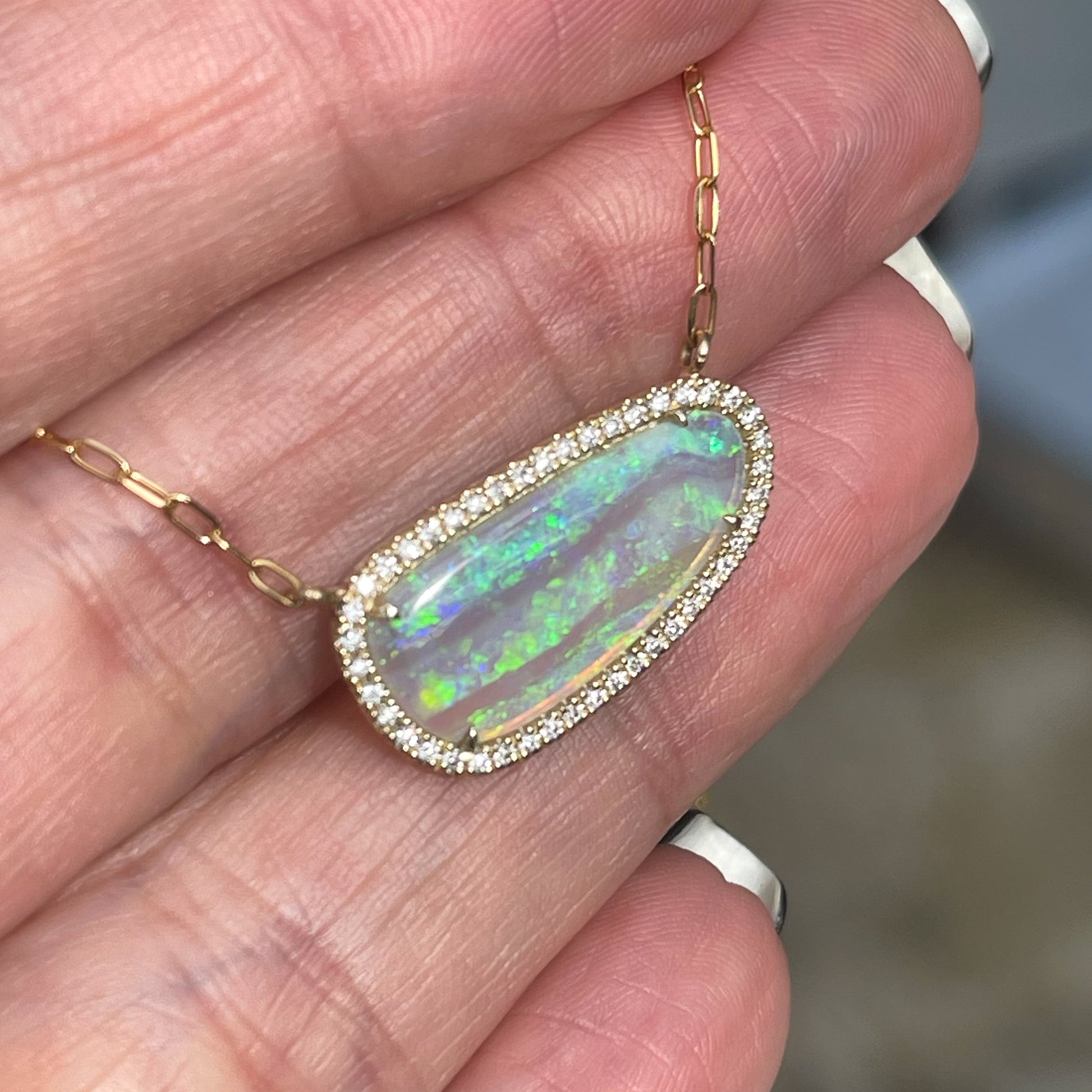 Angled shot of an Australian Opal Necklace by NIXIN Jewelry set in yellow gold with a diamond halo and a paperclip chain.