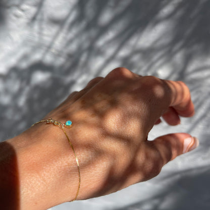 An Australian Opal Bracelet by NIXIN Jewelry modeled on the wrist. A gold opal bracelet with a small blue opal.