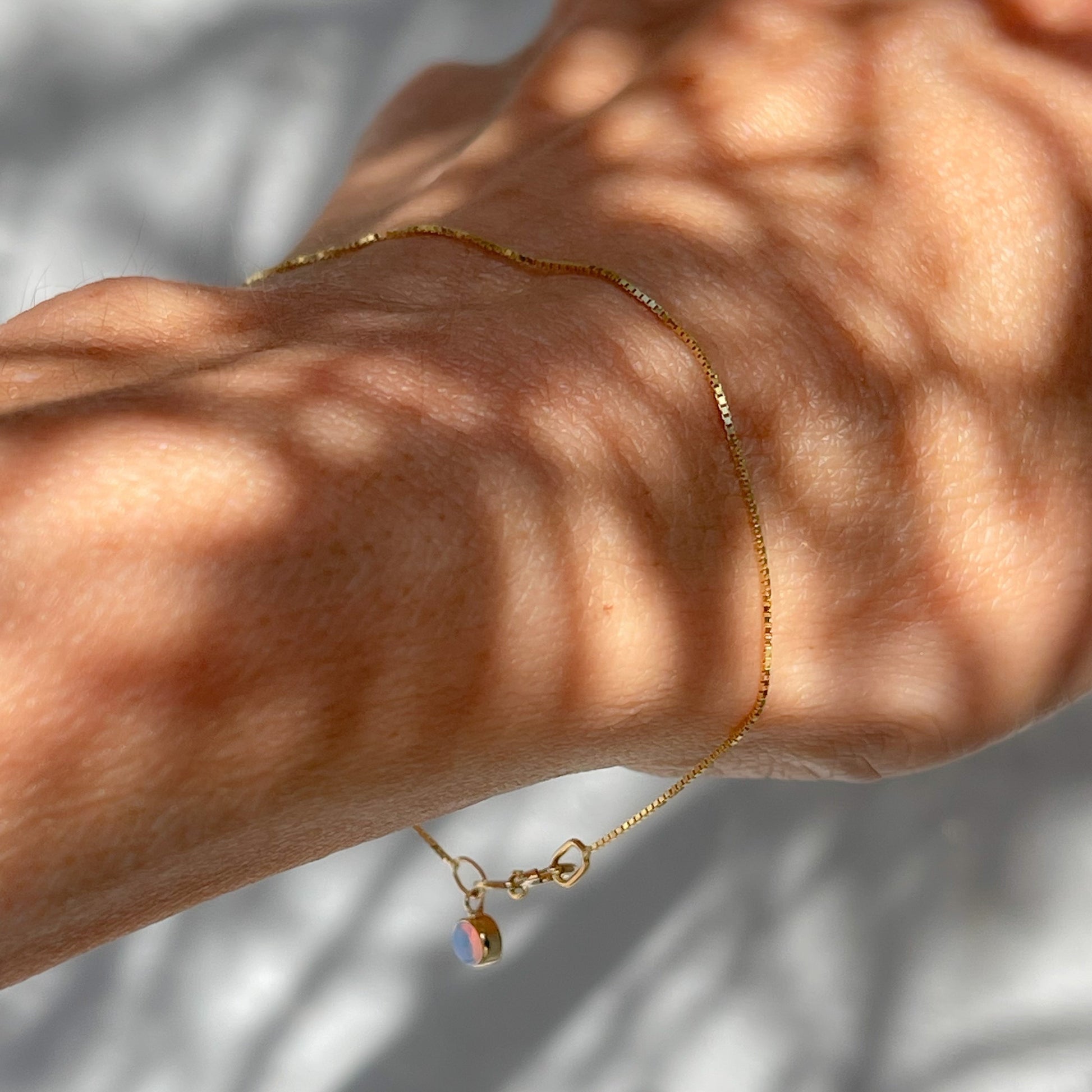 An Australian Opal Bracelet by NIXIN Jewelry worn by a model and shown in shade. A sweet opal charm bracelet.