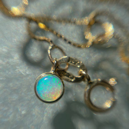 A close up of an Australian Opal Bracelet by NIXIN Jewelry resting on a table. The gold opal bracelet has a natural opal charm.