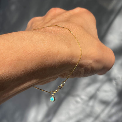 An Australian Opal Bracelet by NIXIN Jewelry shown on a model's wrist. The gold box chain suspends the opal charm and makes a delicate gold bracelet.