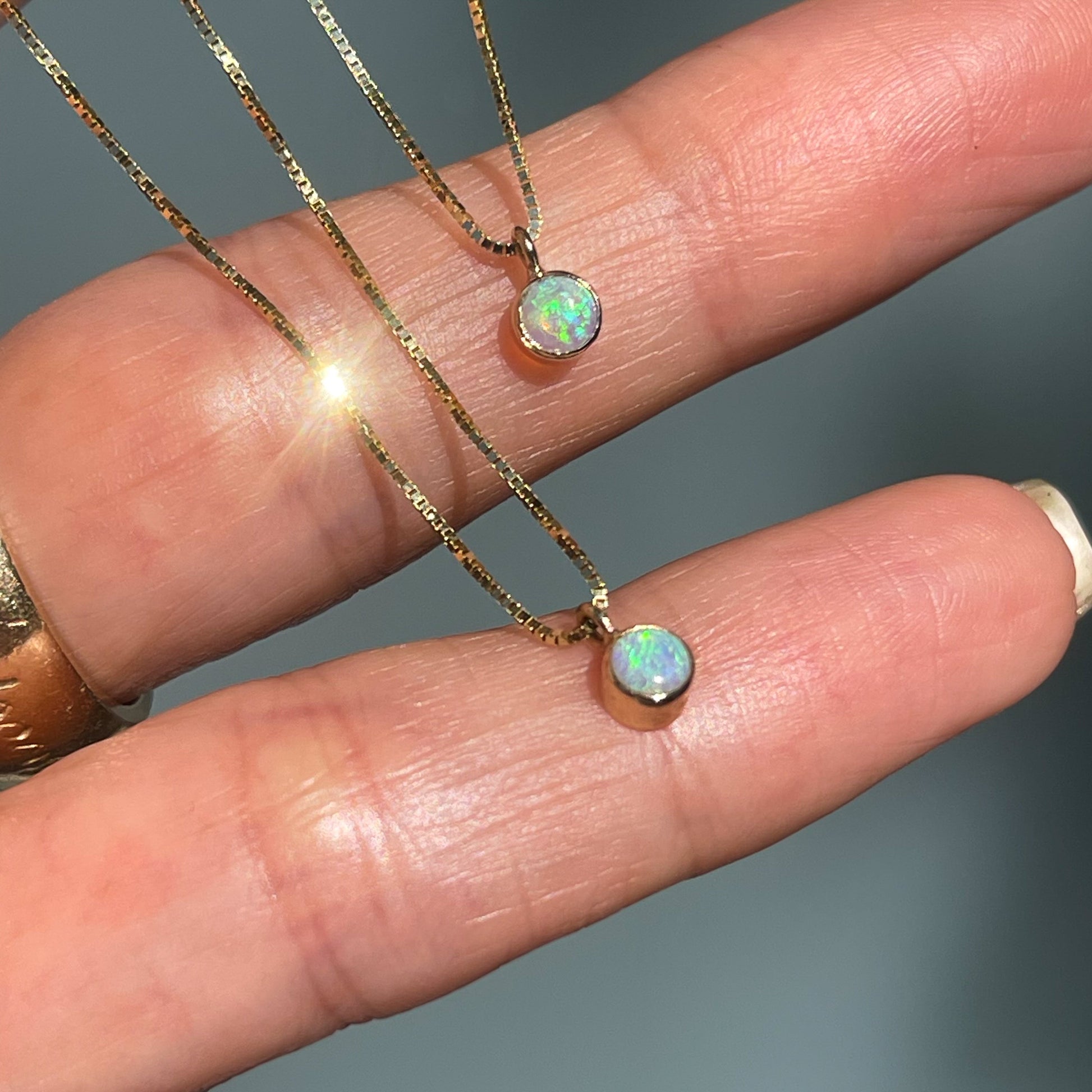 Two Australian Opal Necklaces by NIXIN Jewelry rest atop a hand. The dainty gold chains shine bright and dangle small green opal charms.