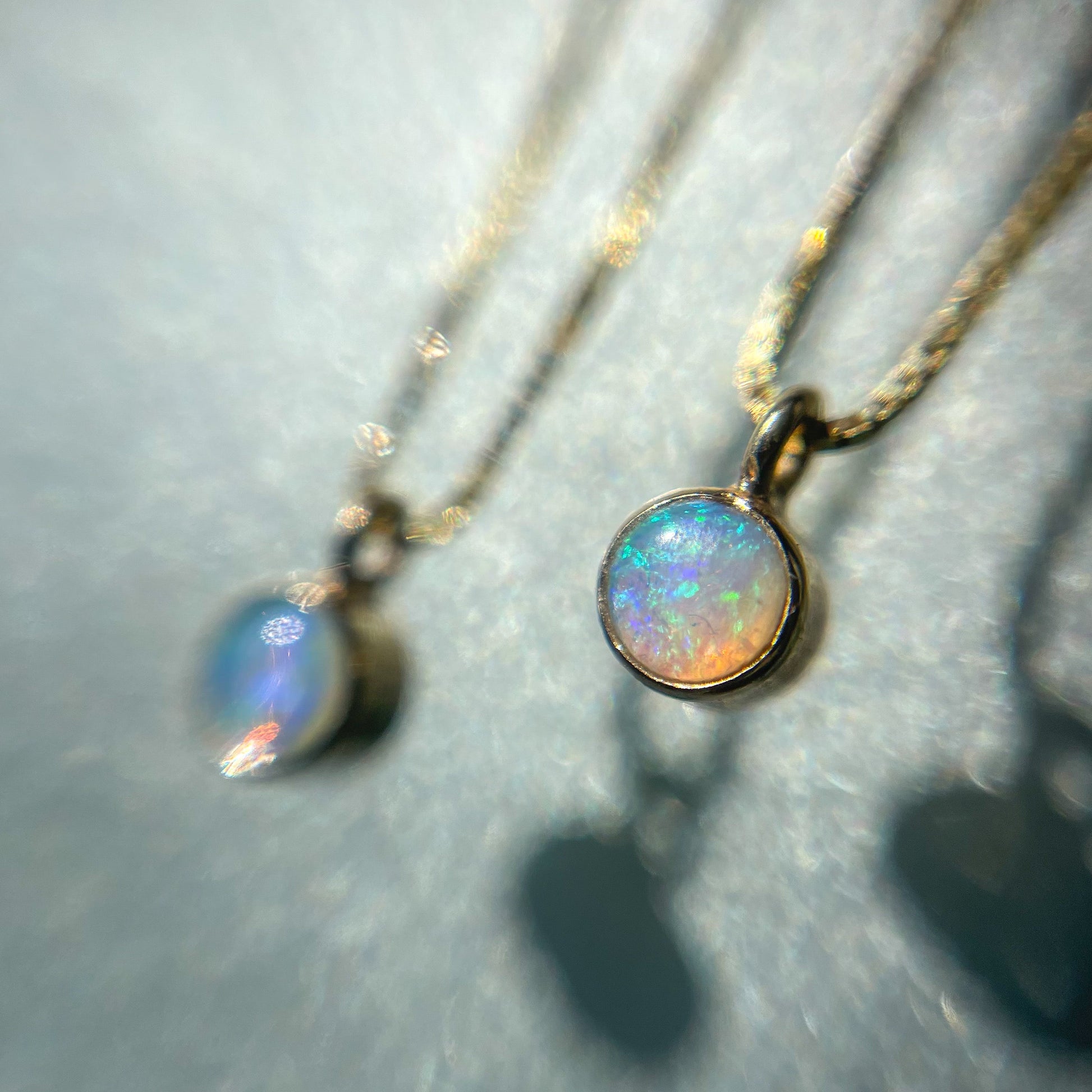 Two Australian Opal Necklaces by NIXIN Jewelry against a glass backdrop. The Crystal Opal Pendant is set in 14k gold.