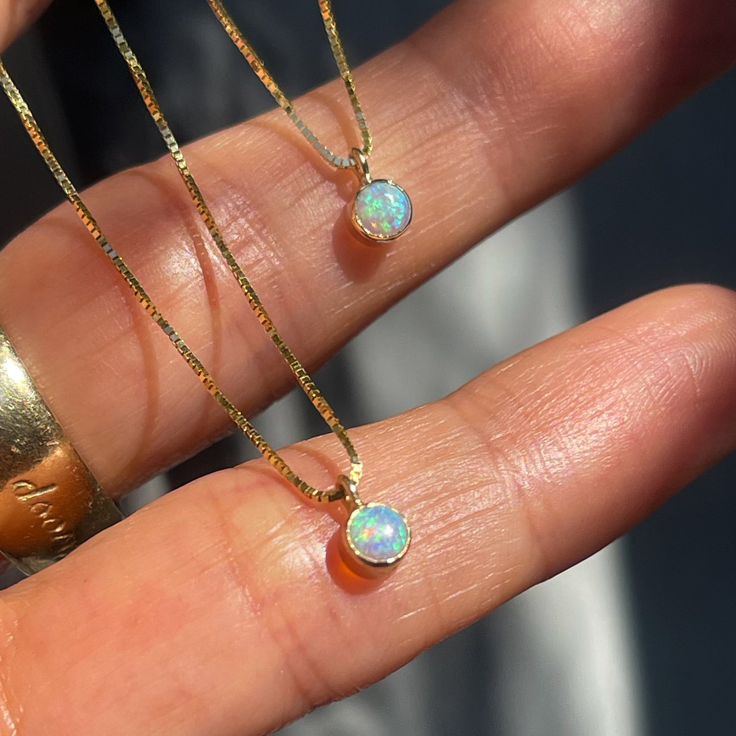 Two Australian Opal Necklaces by NIXIN Jewelry rest upon a hand. The Crystal Opals are fixed in bezel settings that slide along a 16" chain.
