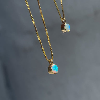 A side view of two Australian Opal Necklaces by NIXIN Jewelry in front of a grey backdrop.The opal pendants hang from beautiful gold box chains.