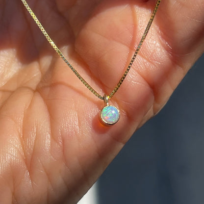 An Australian Opal Necklace by NIXIN Jewelry rests atop a hand. The Crystal Opal necklace has a small opal charm.