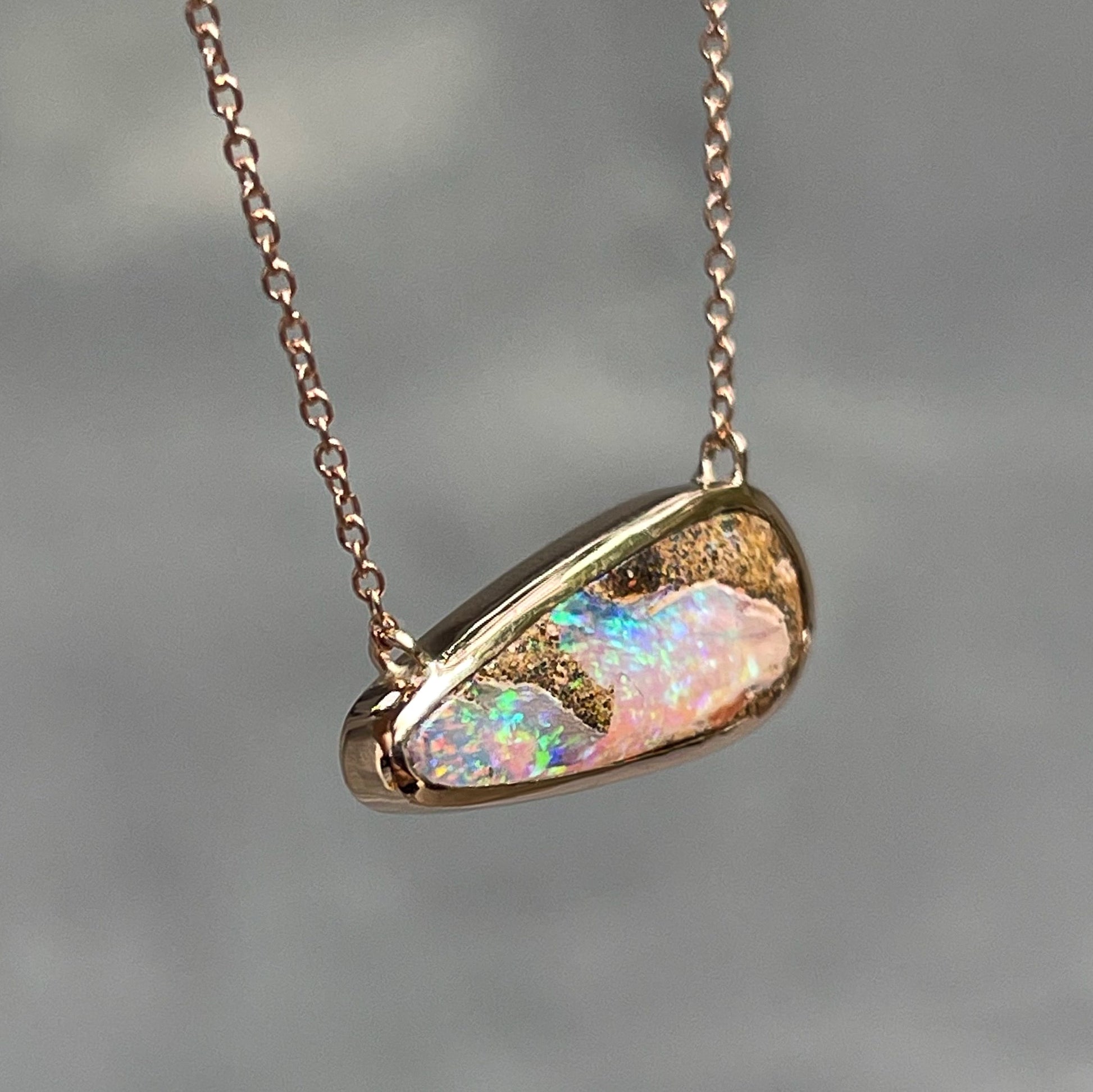 An angled shot of Australian Opal Necklace by NIXIN Jewelry showing the top of the bezel setting. The opal pendant in made in rose gold.