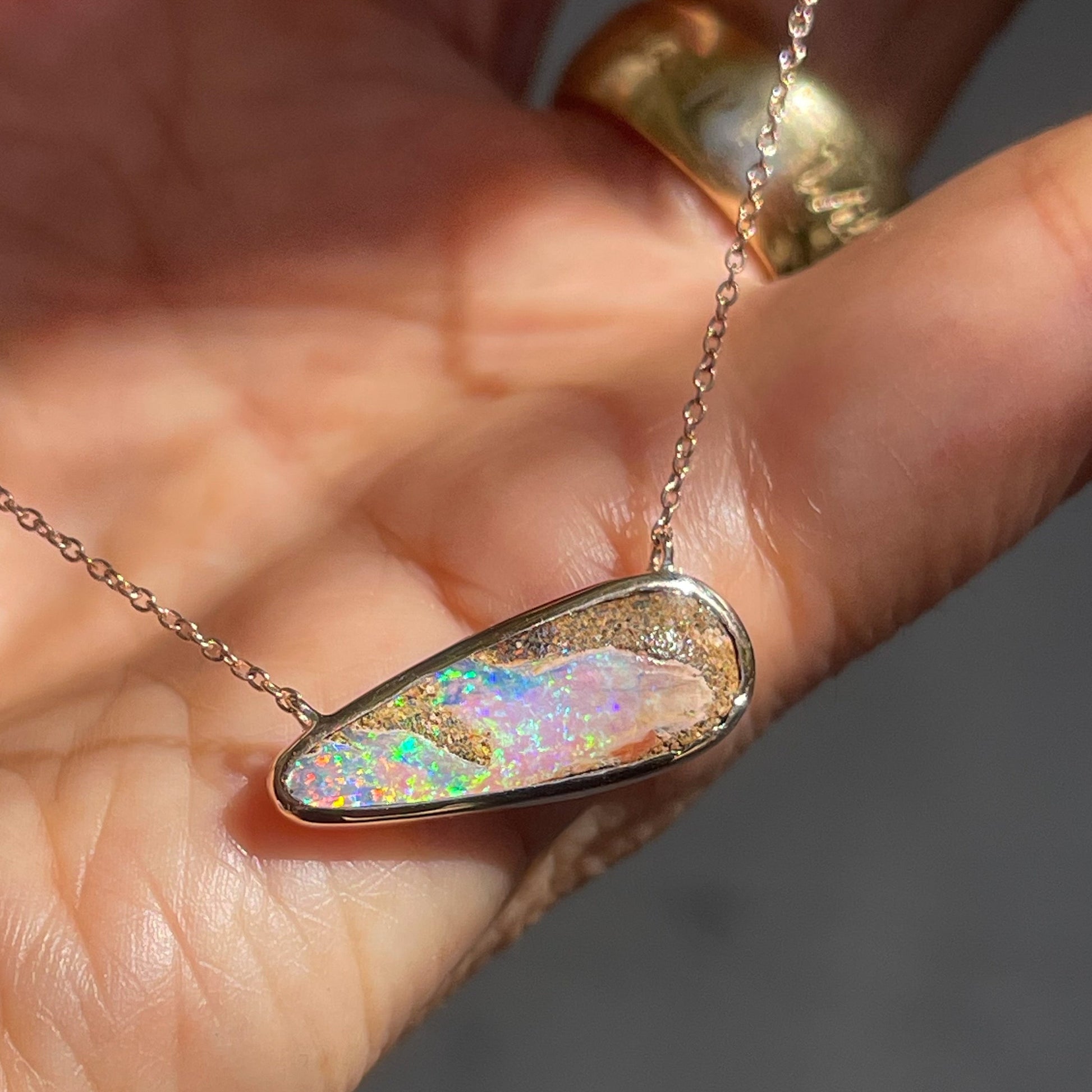 An Australian Opal Necklace by NIXIN Jewelry resting on the palm of a hand. The Australian Opal stone is elongated and displays both host stone and precious Crystal Opal on its face.