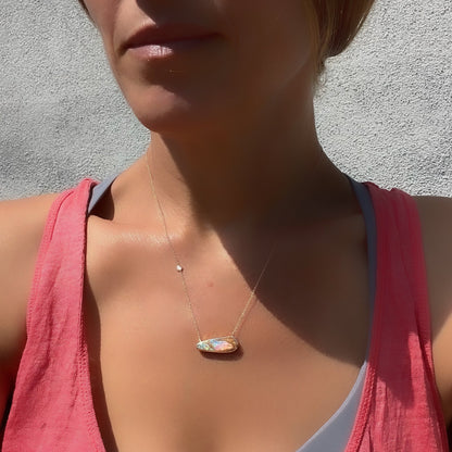 An Australian Opal Necklace by NIXIN Jewelry on a model. The rose gold opal necklace shows off its sparkling diamond and pink and green opal in the sunlight.