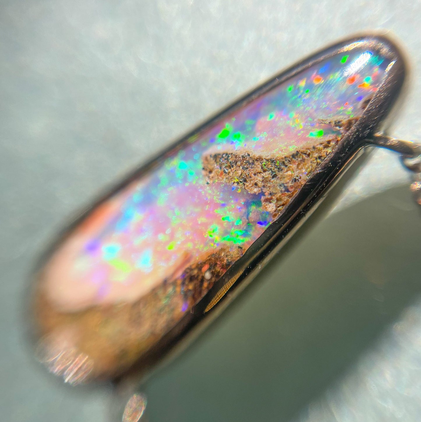 A magnified shot of an Australian Opal Necklace by NIXIN Jewelry. The pink opal sparkles with vibrant greens and blues all across its facade.