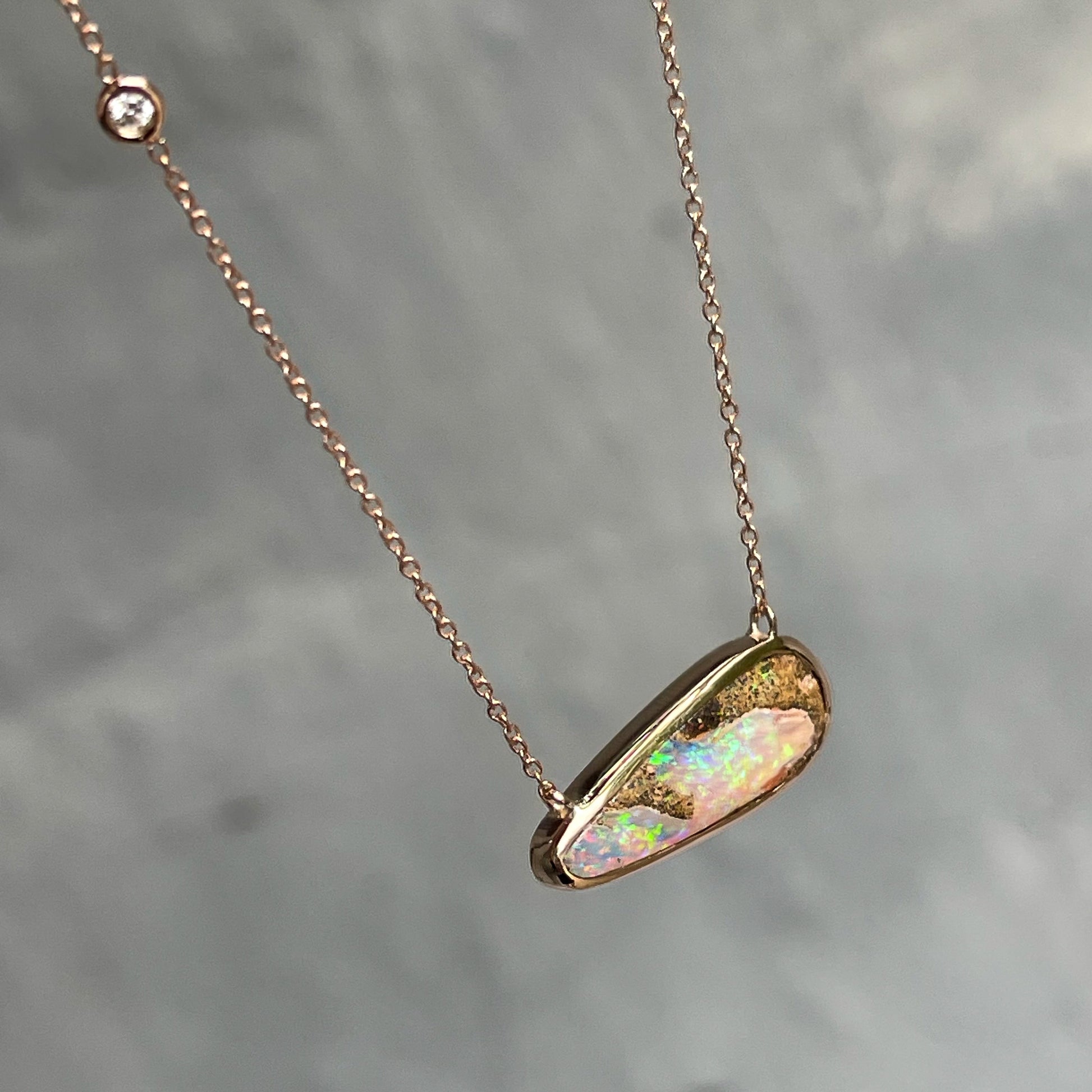 An Australian Opal Necklace by NIXIN Jewelry shot from above showing the top of its bezel and the diamond set into its chain. The 14k rose gold opal pendant necklace is 18" long with a 17" adjuster.