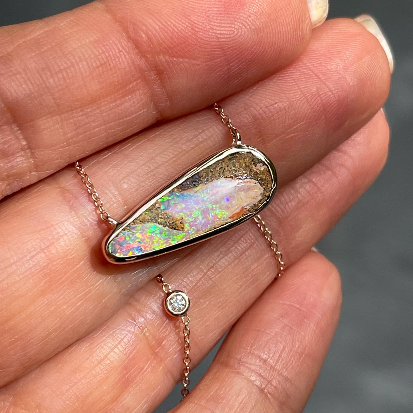 An Australian Opal Necklace by NIXIN Jewelry staged upon a hand. The pipe opal necklace is oriented horizontally and has a diamond in the delicate chain.