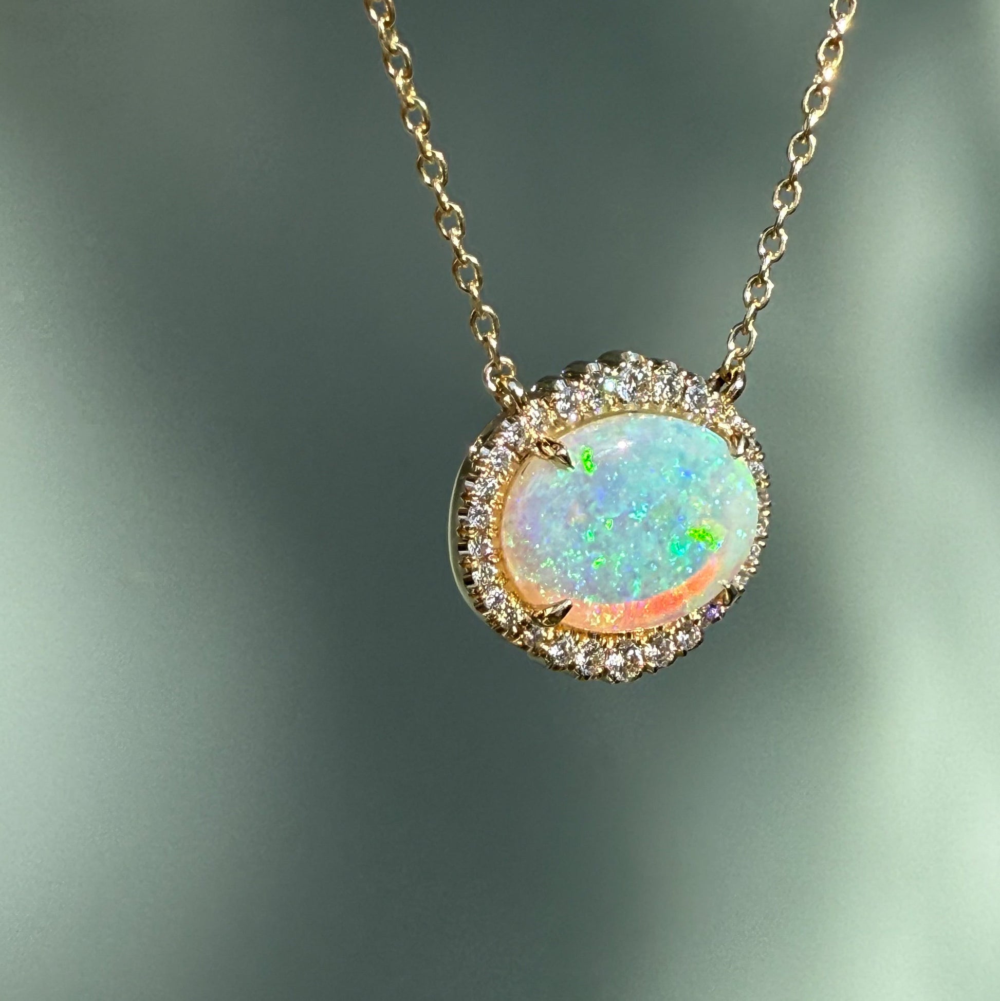 An Australian Opal Necklace by NIXIN Jewelry, highlighting the intense play-of-color in a natural opal. This unique opal jewelry piece features an oval opal stone with a shimmering diamond halo, hanging at an angle. An exquisite women's luxury necklace and rare opal jewelry offering.