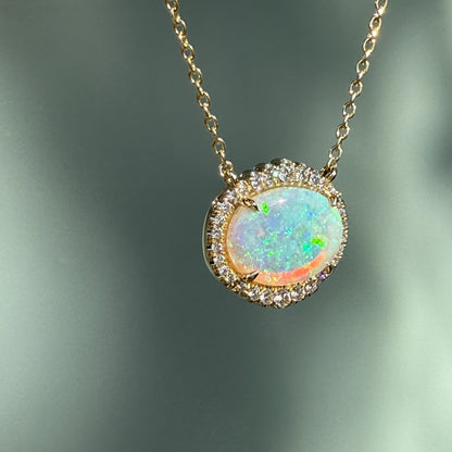 An Australian Opal Necklace by NIXIN Jewelry, highlighting the intense play-of-color in a natural opal. This unique opal jewelry piece features an oval opal stone with a shimmering diamond halo, hanging at an angle. An exquisite women's luxury necklace and rare opal jewelry offering.