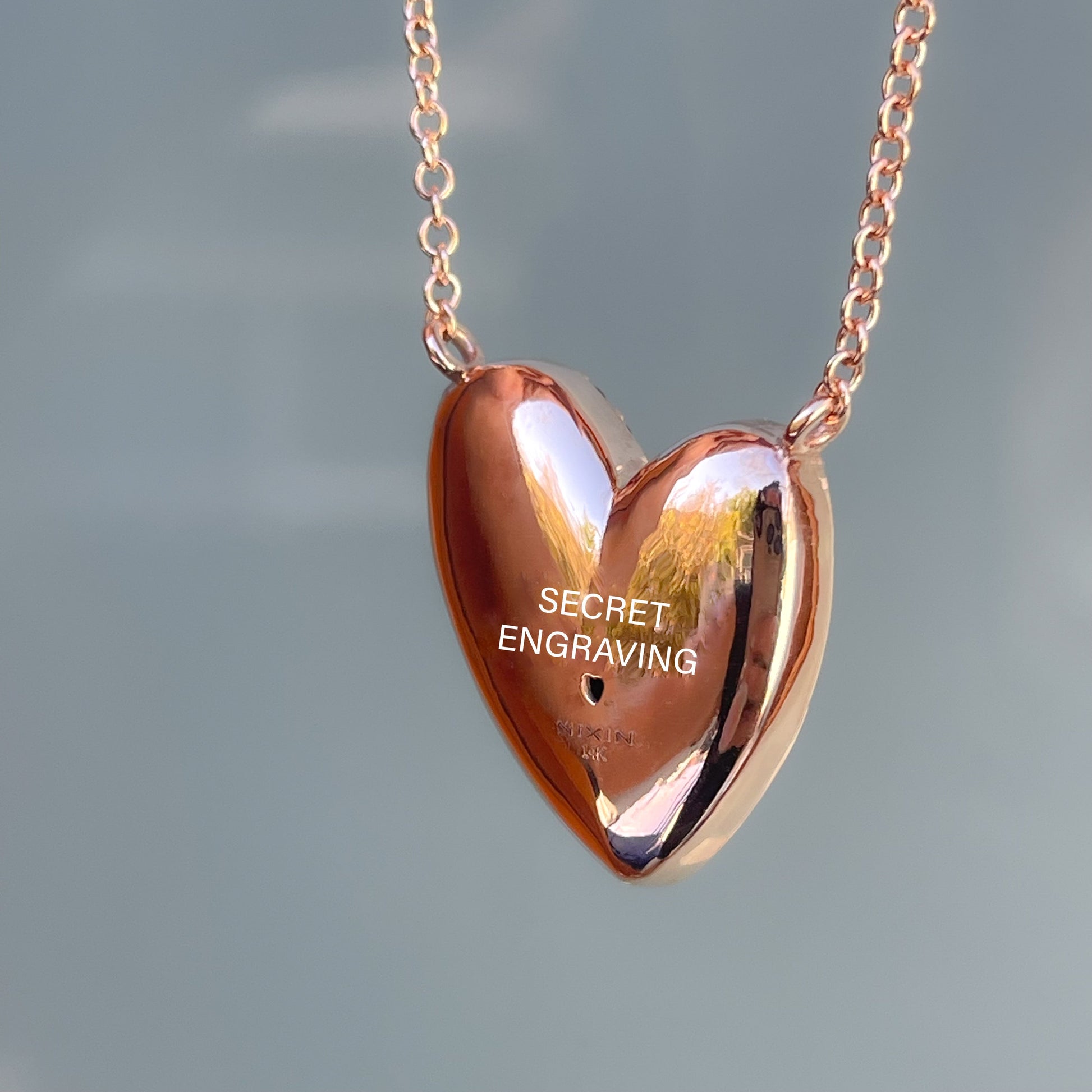 The back of a Heart Opal Necklace by NIXIN Jewelry showing the rose gold encasing, heart cutout, and location of the secret engraving.