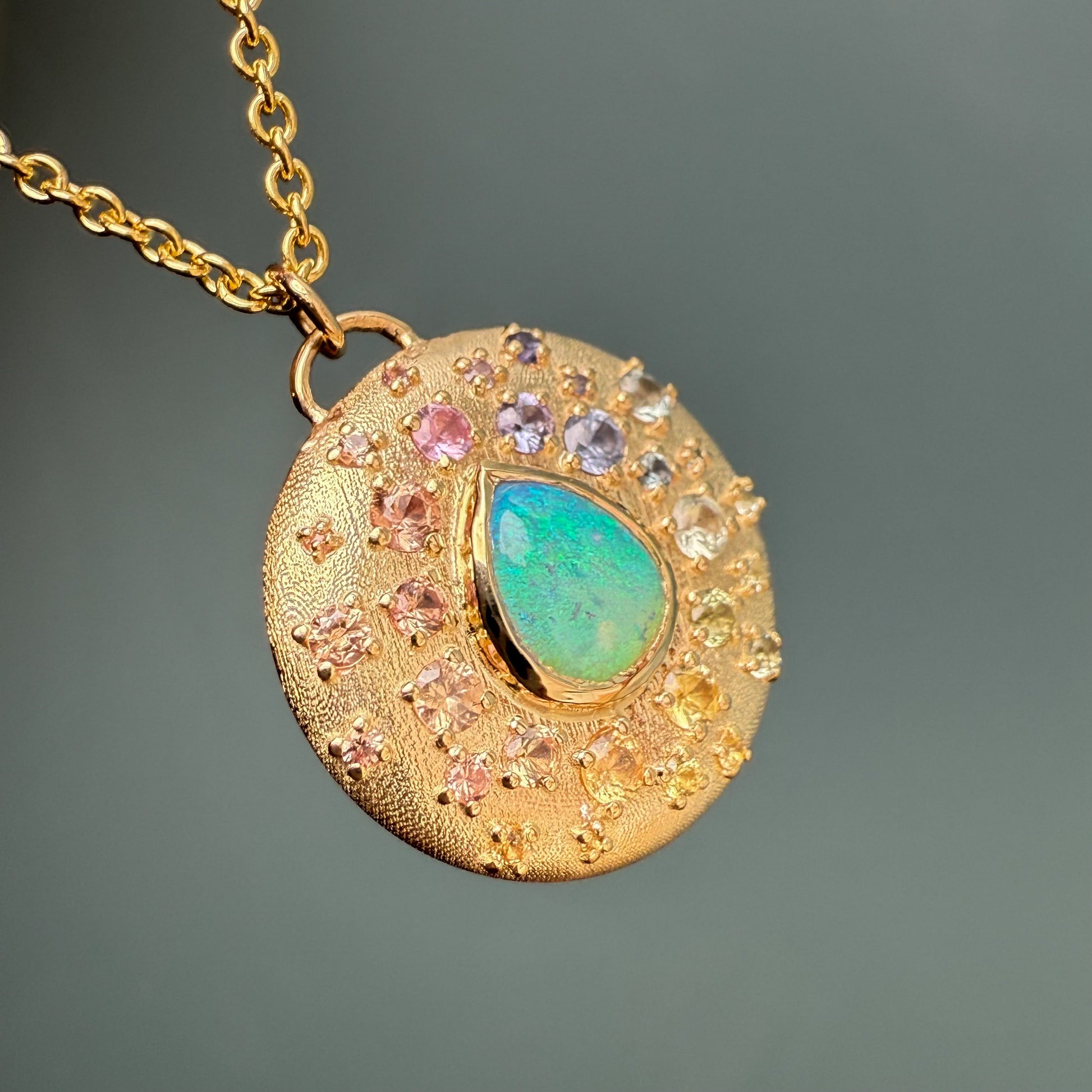An Australian Opal Necklace by NIXIN Jewelry displays a central opal surrounded by a scattering of sapphires. This luxury necklace features bead-set gems in varied sizes and rainbow hues.