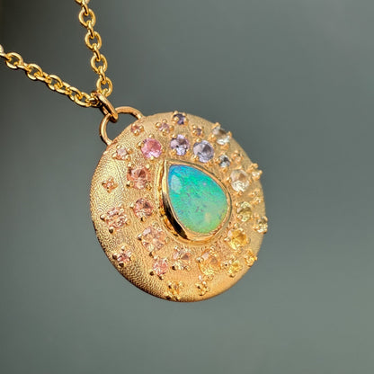An Australian Opal Necklace by NIXIN Jewelry displays a central opal surrounded by a scattering of sapphires. This luxury necklace features bead-set gems in varied sizes and rainbow hues.