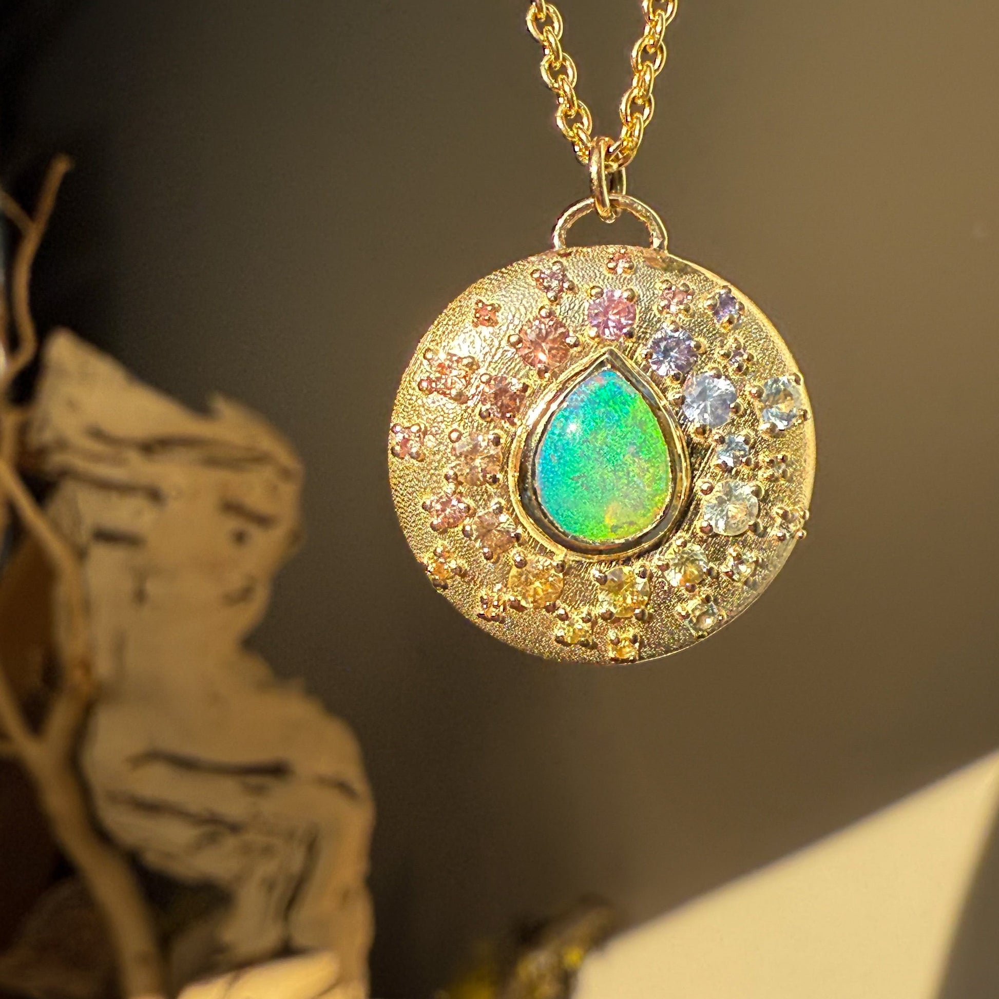 An Australian Opal Necklace by NIXIN Jewelry is a beautiful example of australian opal jewelry. This opal necklace highlights a textured gold disc adorned with a spray of ombré sapphires.
