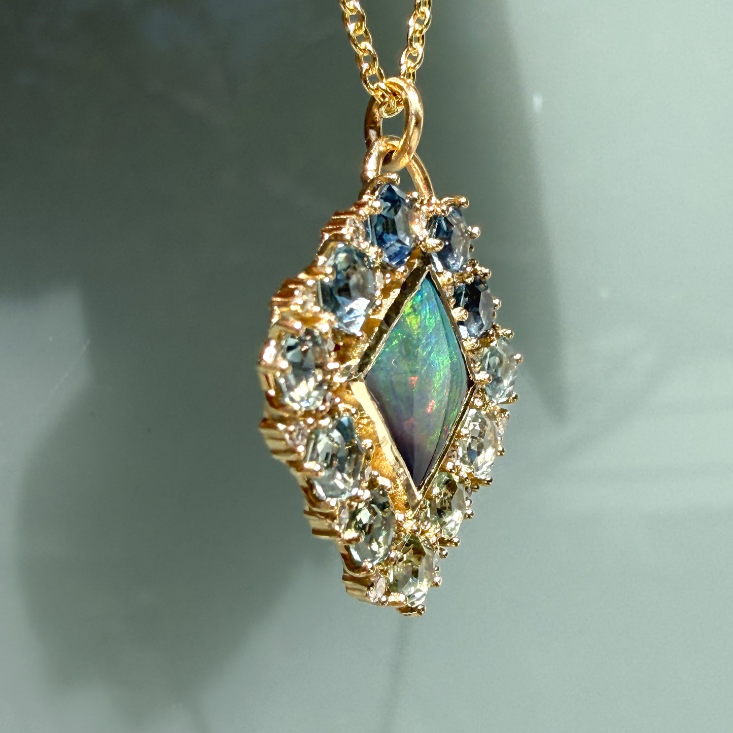 A profile shot captures the dimensional side view of an Australian Opal Pendant by NIXIN Jewelry. This perspective highlights the substantial thickness of the solid gold opal necklace framework and the secure prong settings across the sapphire necklace border. The clean, structured lines emphasize the exceptional craftsmanship behind this piece of luxury jewelry.