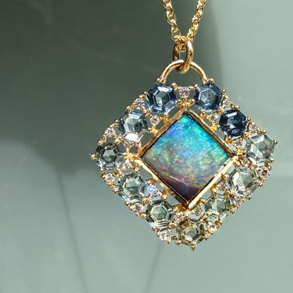 A straight-on view showcases an Australian Opal Pendant by NIXIN Jewelry displaying glowing neon blue and green colors. This gold opal necklace features a premium natural opal center stone from Australia accented by a structural frame of light blue and teal montana sapphires. The exquisite design makes this opal necklace a beautiful work of jewelry art for collectors of rare jewelry.
